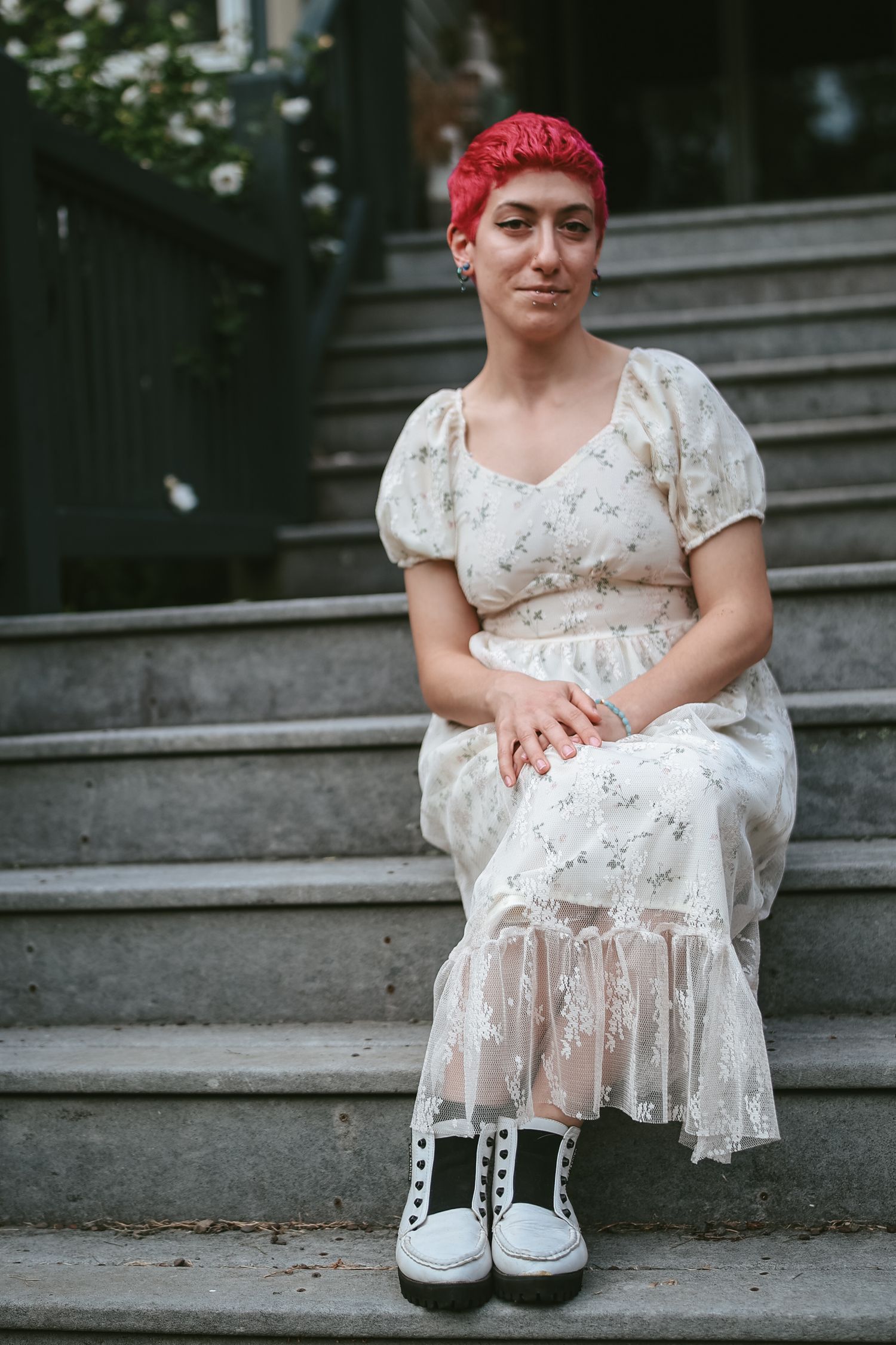 A person in a white floral dress sits on concrete steps wearing black and white sneakers.
