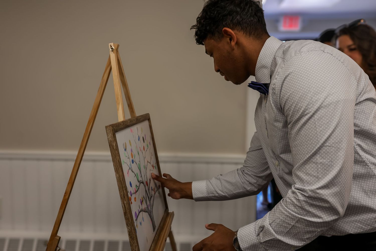 An artist works on a detailed sketch displayed on a wooden easel in an indoor setting.