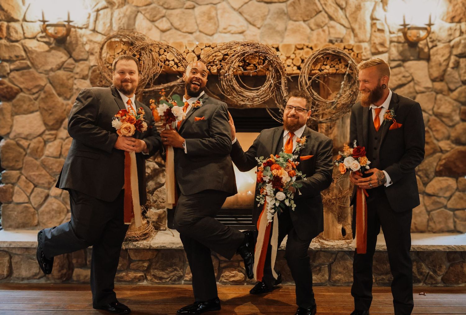 Wedding party members in formal attire hold candles during an indoor ceremony against a stone wall backdrop.