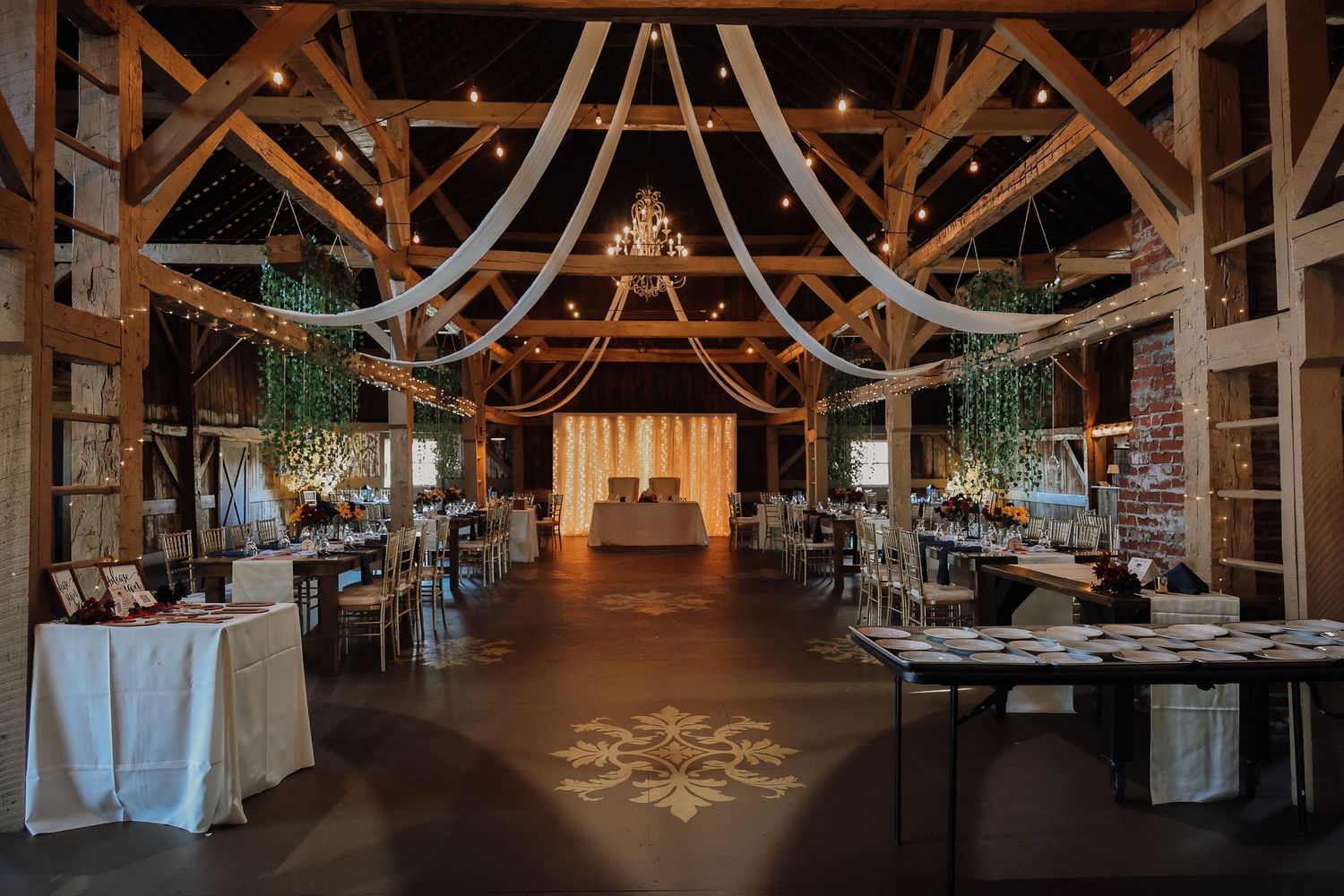 Rustic barn wedding reception venue decorated with white fabric draping and string lights creating an elegant atmosphere.
