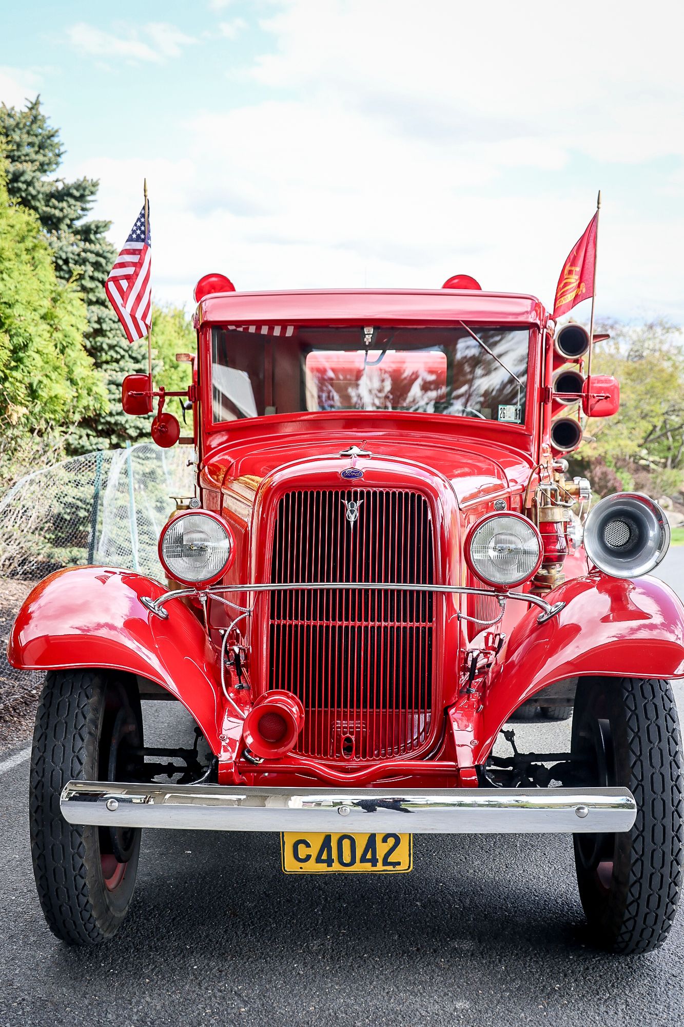 Vintage red fire truck with license plate C4042 and American flag on display outdoors.