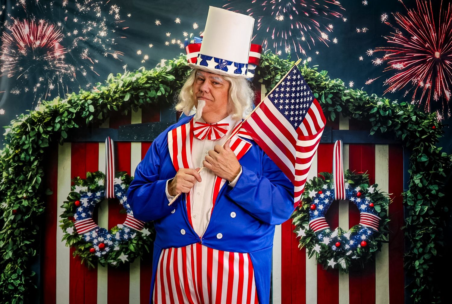Uncle Sam costume character holding American flag with fireworks and patriotic red, white, and blue striped backdrop.