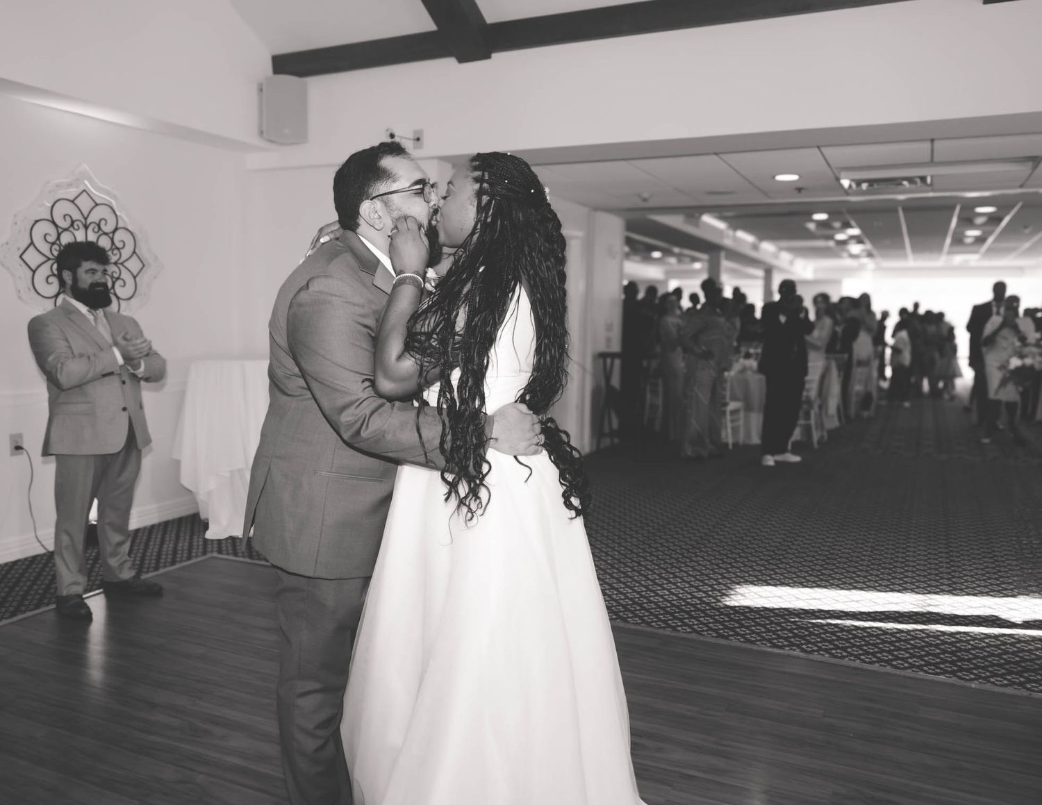 A newlywed couple shares their first dance kiss in a black and white wedding reception photo.