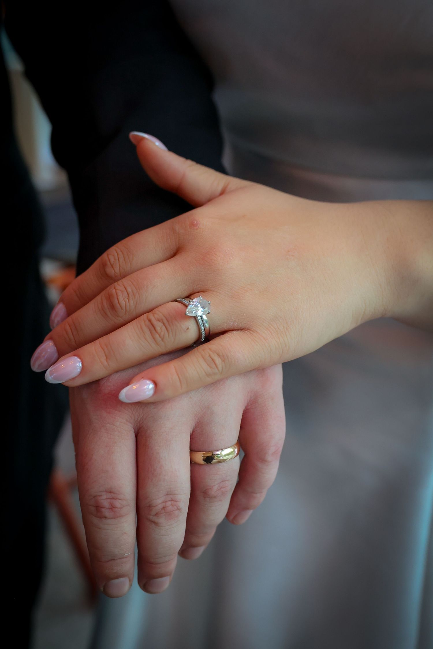 Bride and groom holding hands showing diamond engagement ring and gold wedding band on their fingers.