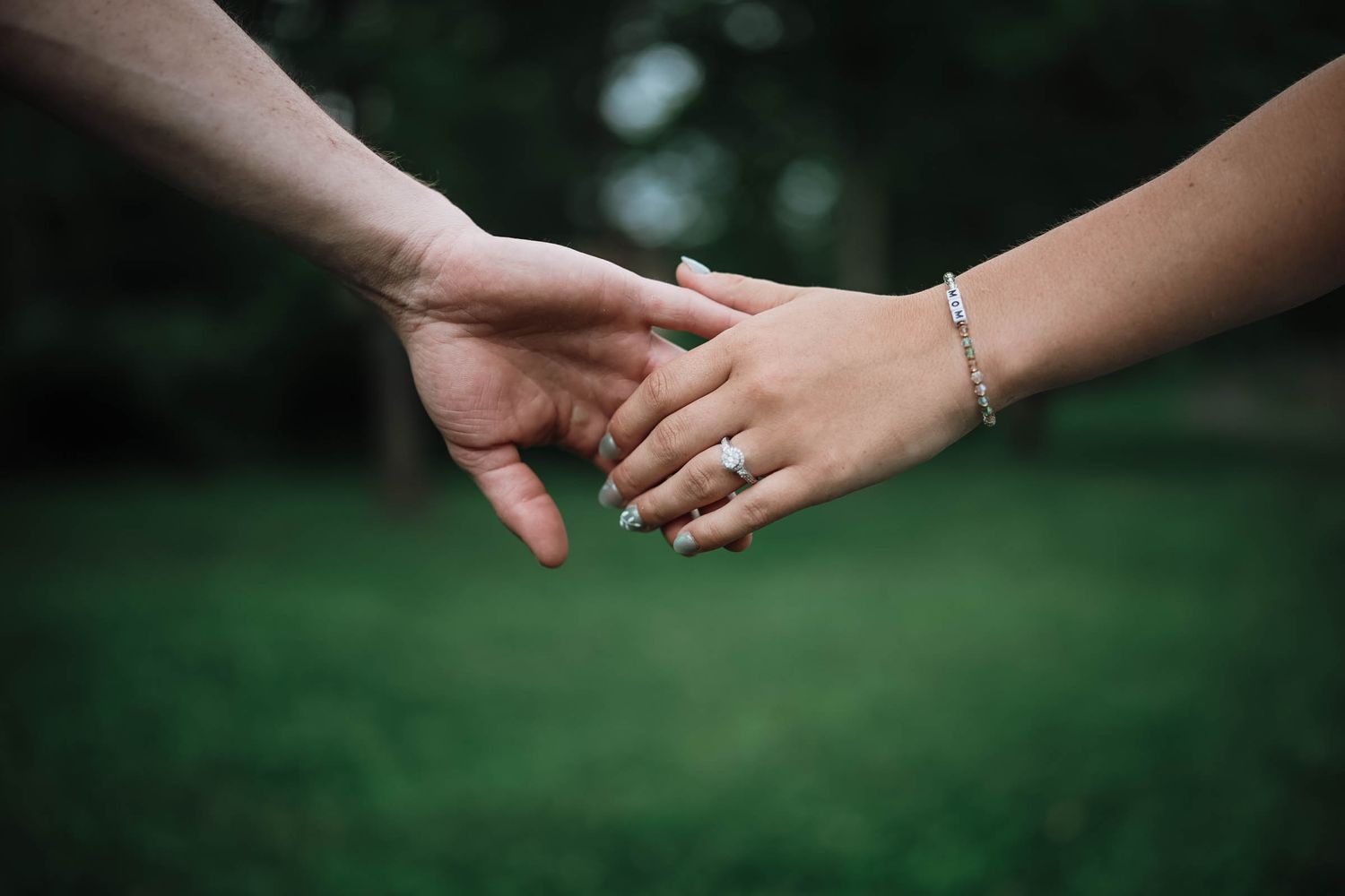 Close-up of couple holding hands, woman wearing a diamond engagement ring and silver bracelet.