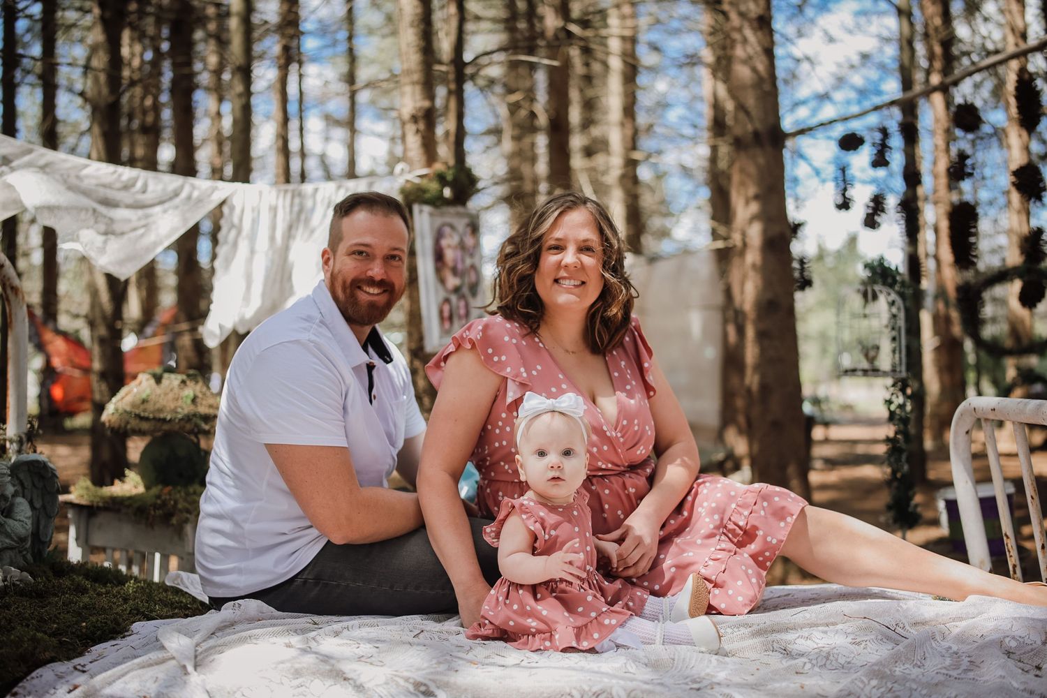 A happy family with a baby girl in pink dresses poses for a portrait in a whimsical forest setting.