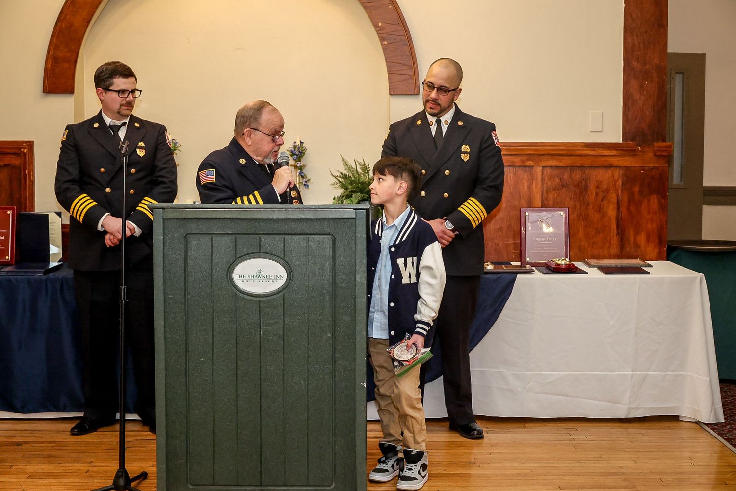 Fire department officers present award to young boy at formal ceremony indoors.