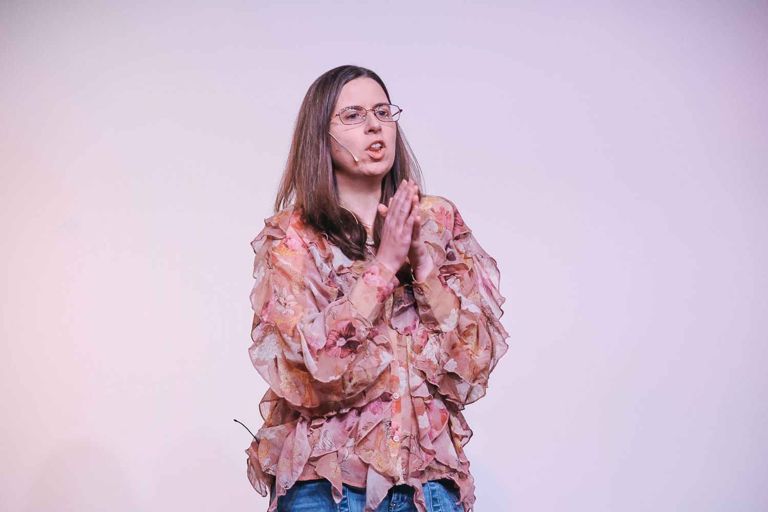 Young person in a ruffled floral blouse with hands pressed together, posing against a light background.
