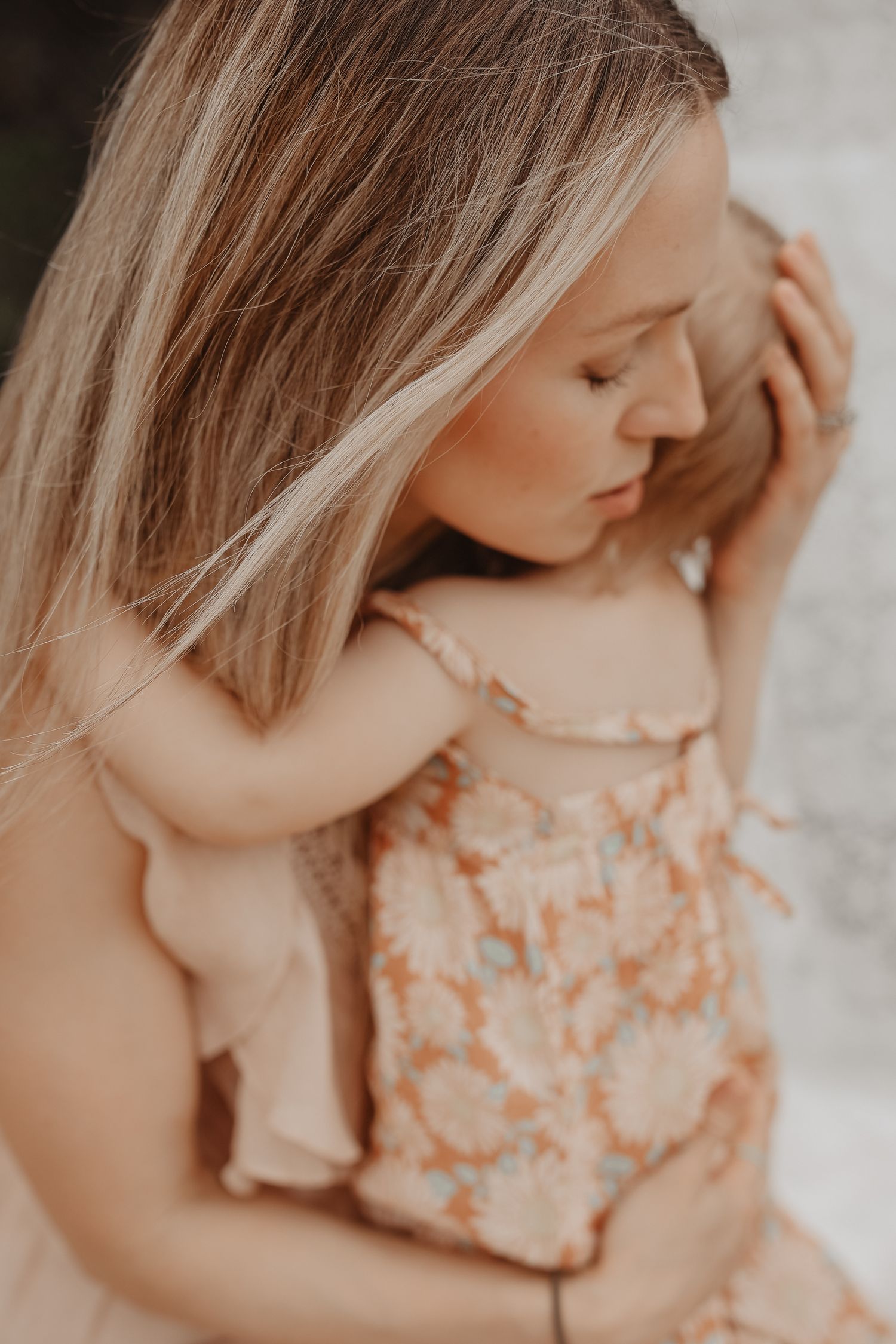 Soft portrait in muted tones showing gentle embrace and blonde hair against floral pattern dress.