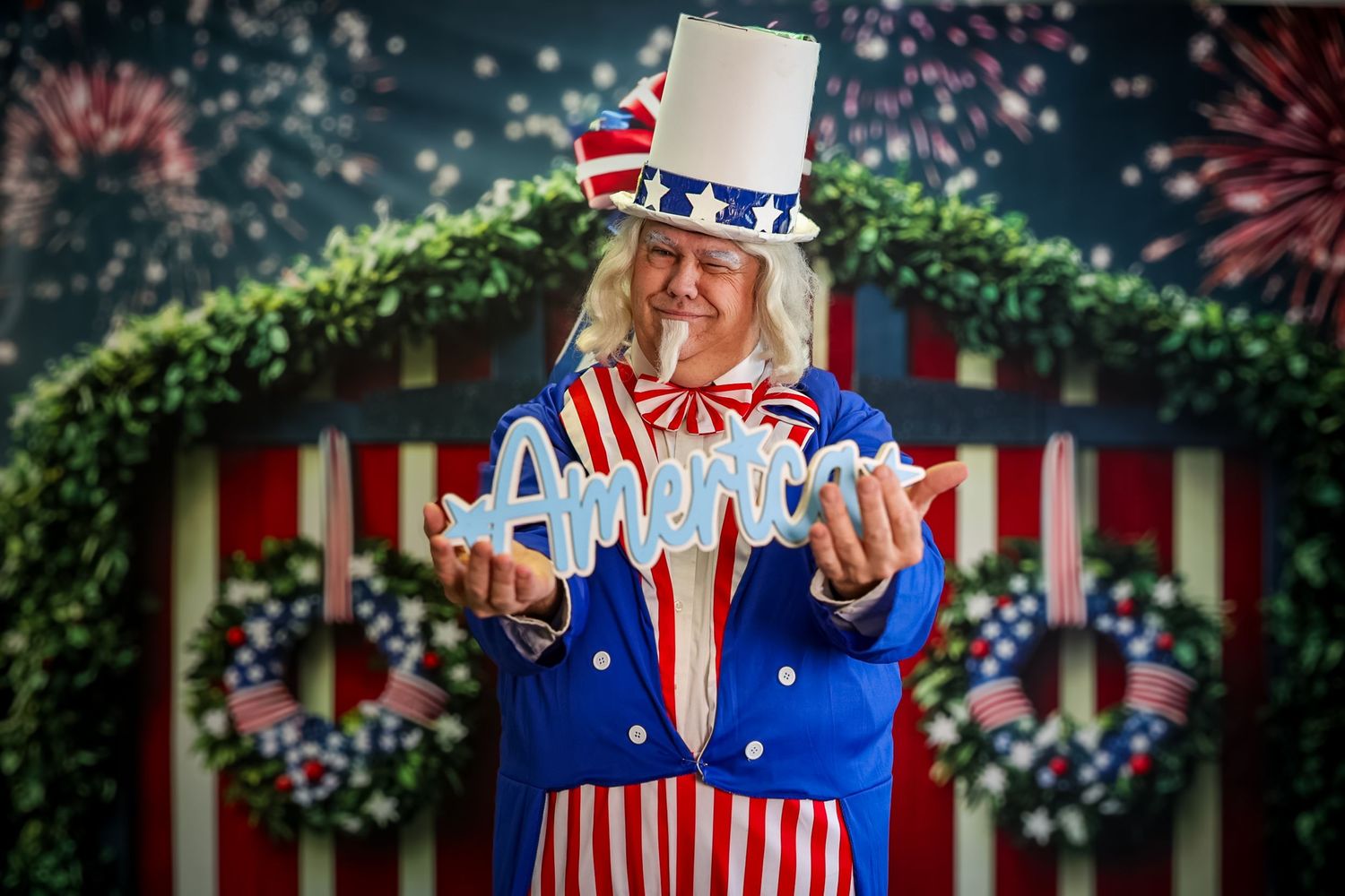 Person dressed as Uncle Sam holding an America sign with fireworks and patriotic decorations in the background.