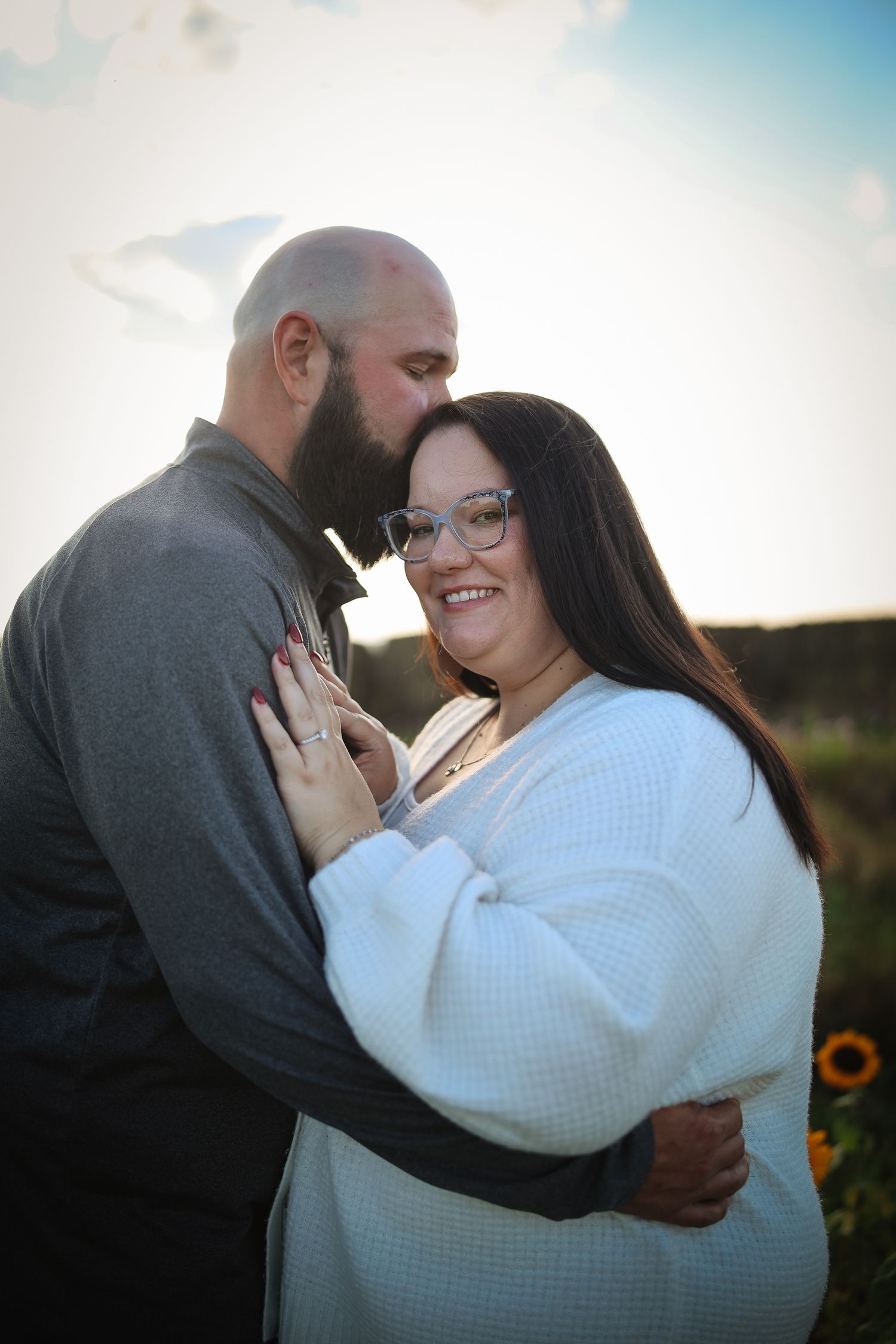 A romantic couple embraces in a sunlit field during a golden hour engagement photo session.