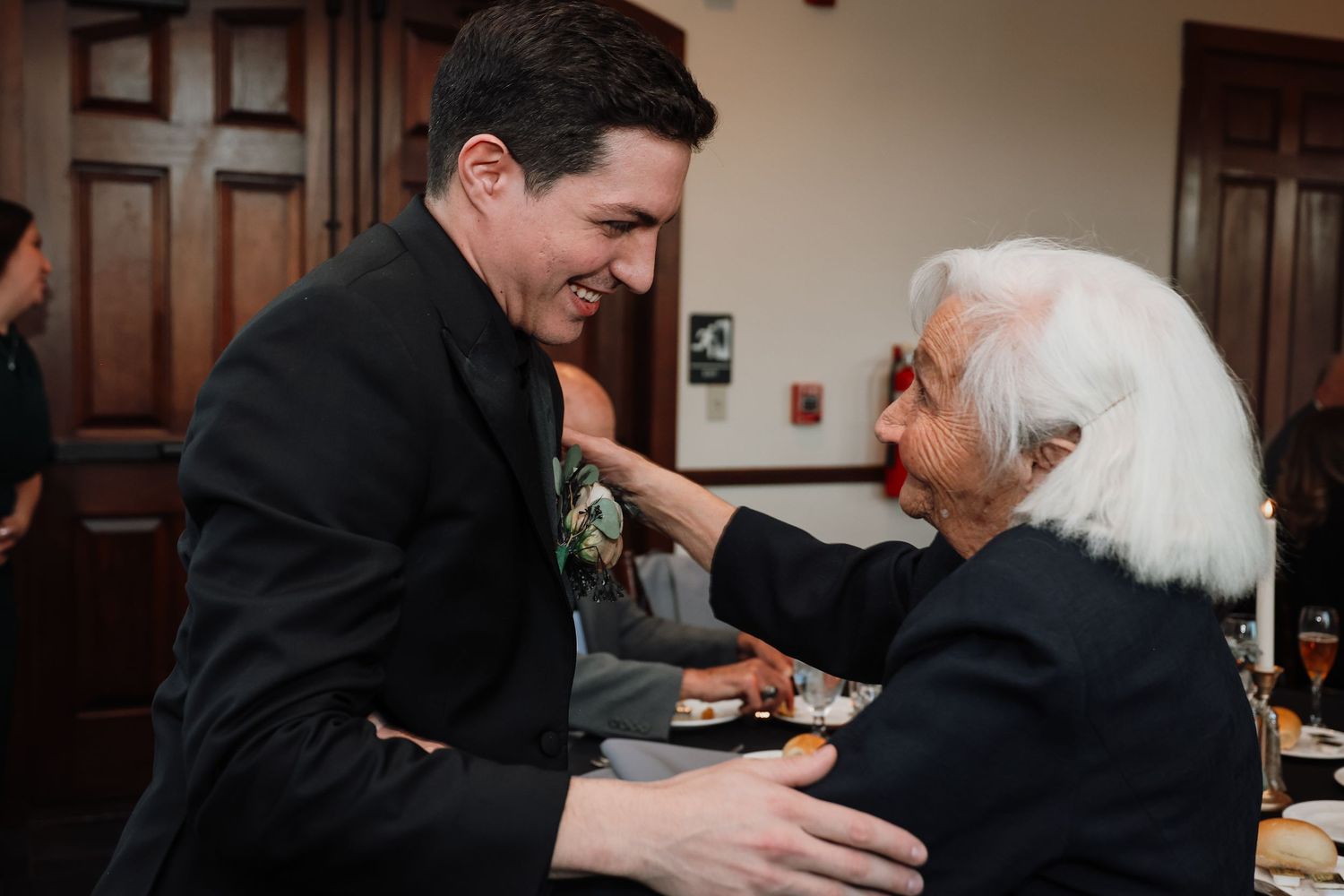 Two people in formal attire share a warm embrace during a celebratory event in an elegant indoor setting.