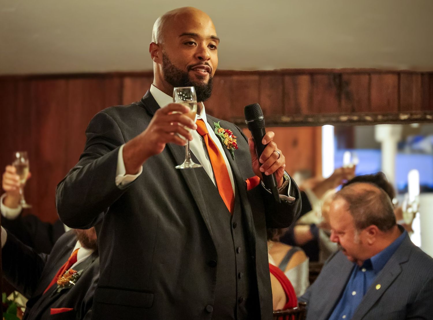 Professional speaker gestures with hands while giving presentation in wood-paneled conference room.