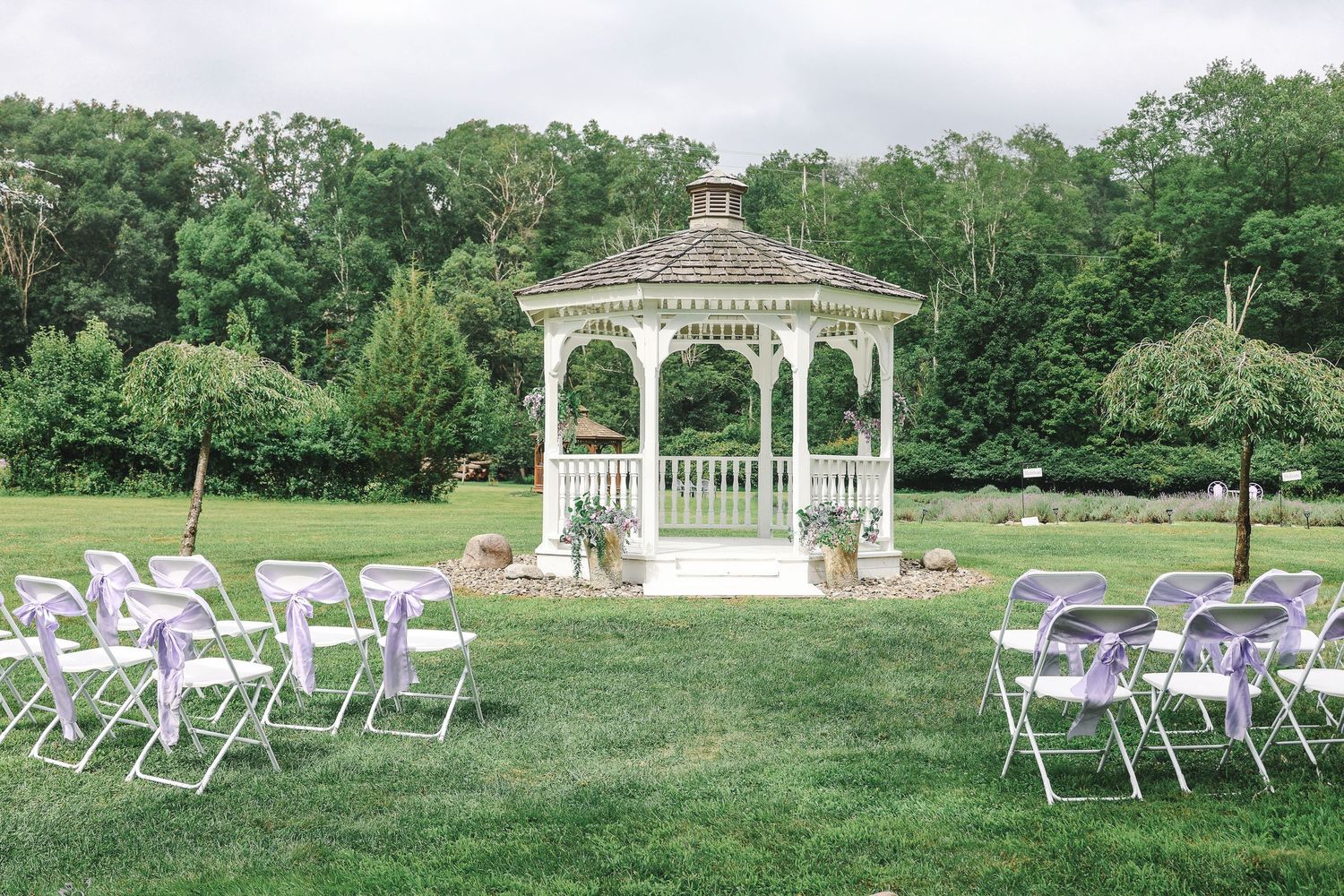 White folding chairs arranged in rows on a green lawn facing an elegant white gazebo for an outdoor wedding ceremony.