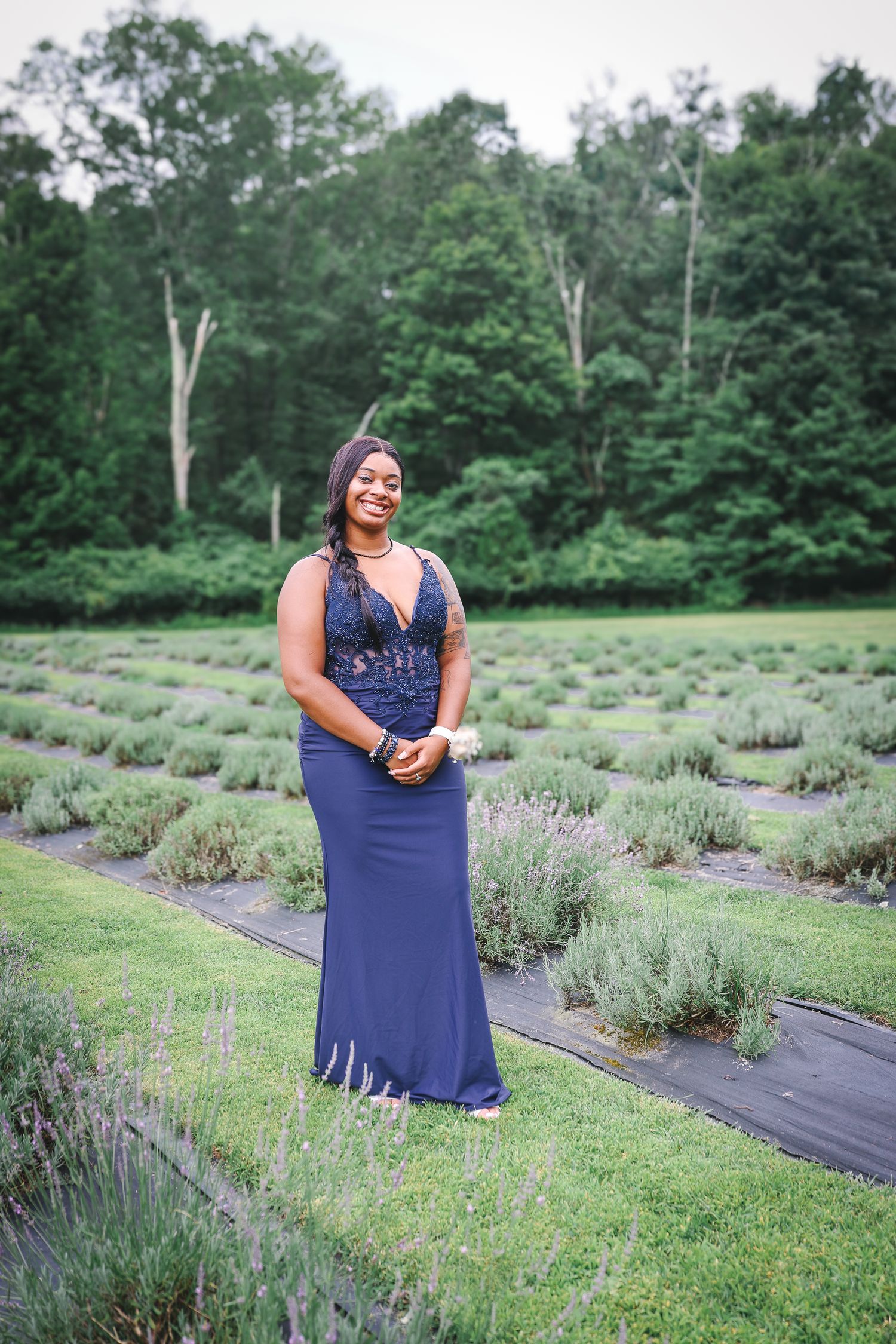 A woman in a navy dress walks through rows of fragrant lavender plants in a peaceful garden setting.