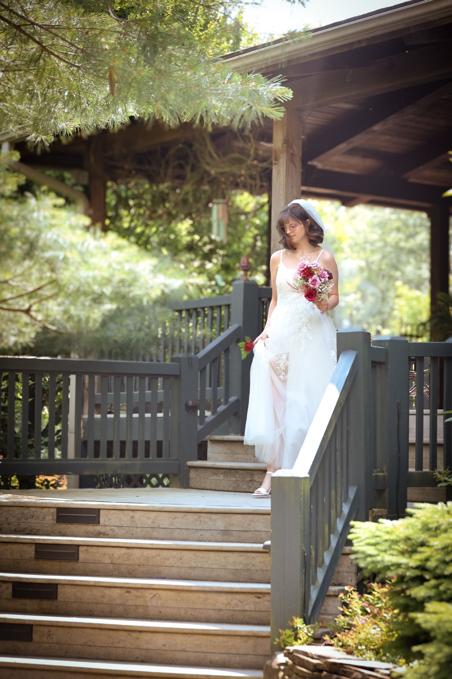 A couple shares a tender moment on wooden steps of a covered porch surrounded by lush greenery.