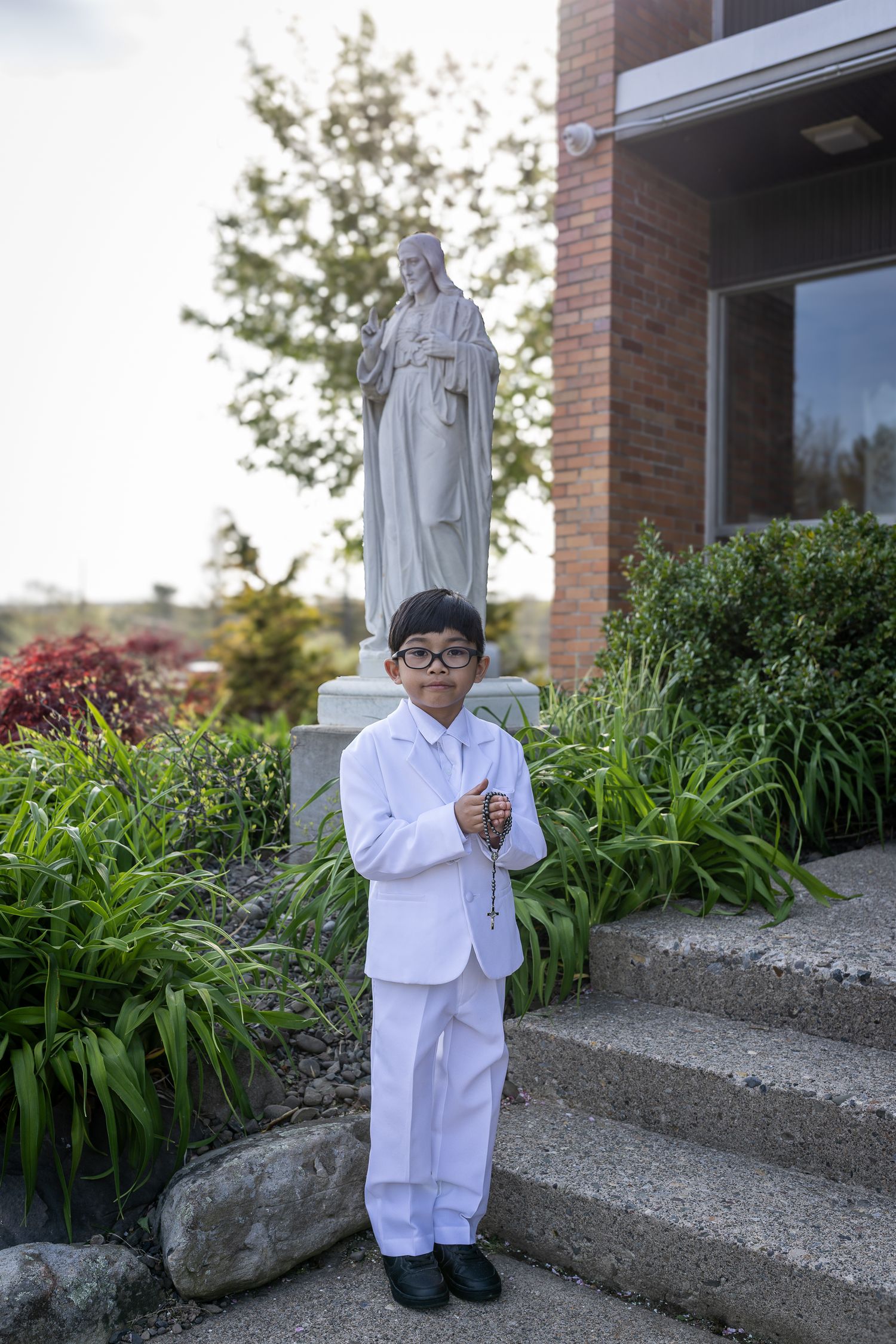 A figure in a white suit and glasses stands on concrete steps near landscaped greenery in a series of four photos.