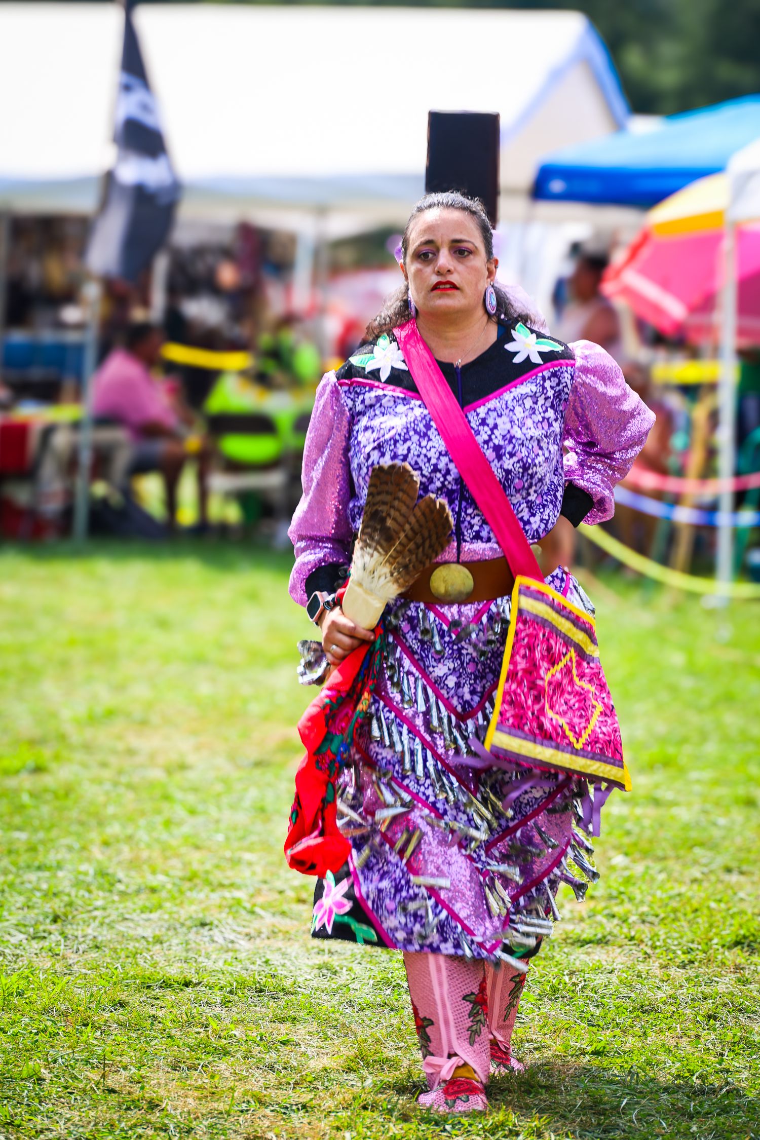 Dancers in vibrant pink and purple regalia perform traditional Native American dances at an outdoor powwow festival.