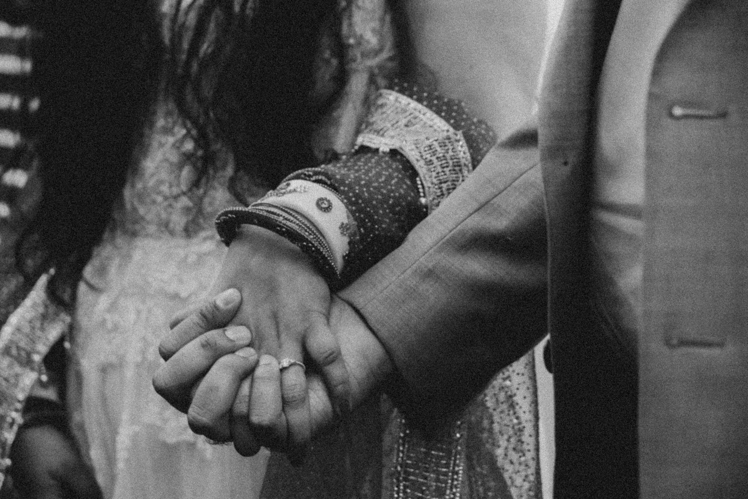 Black and white close-up photo of two people holding hands, with one wearing lace or delicate fabric.