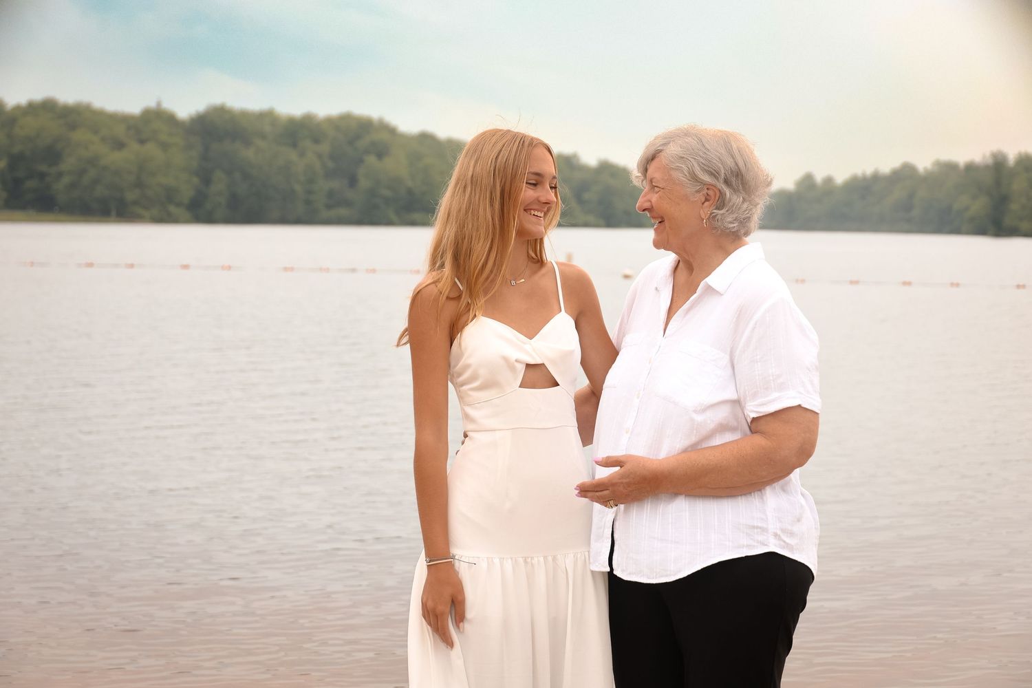 Two people in light colored clothing share romantic moments by a serene lakeside at sunset.