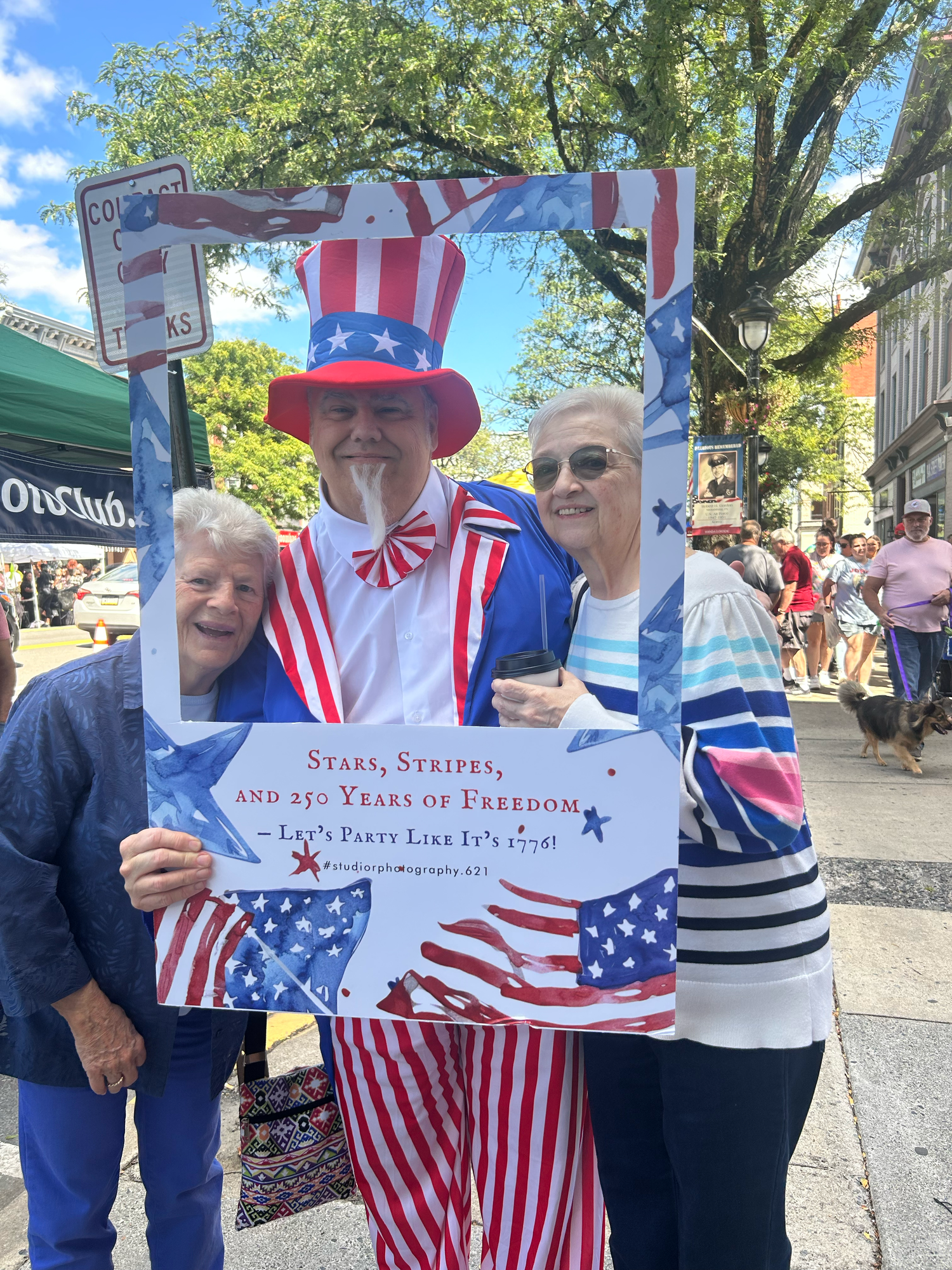 A group displays patriotic American flags and decorations at an outdoor gathering under sunny skies.