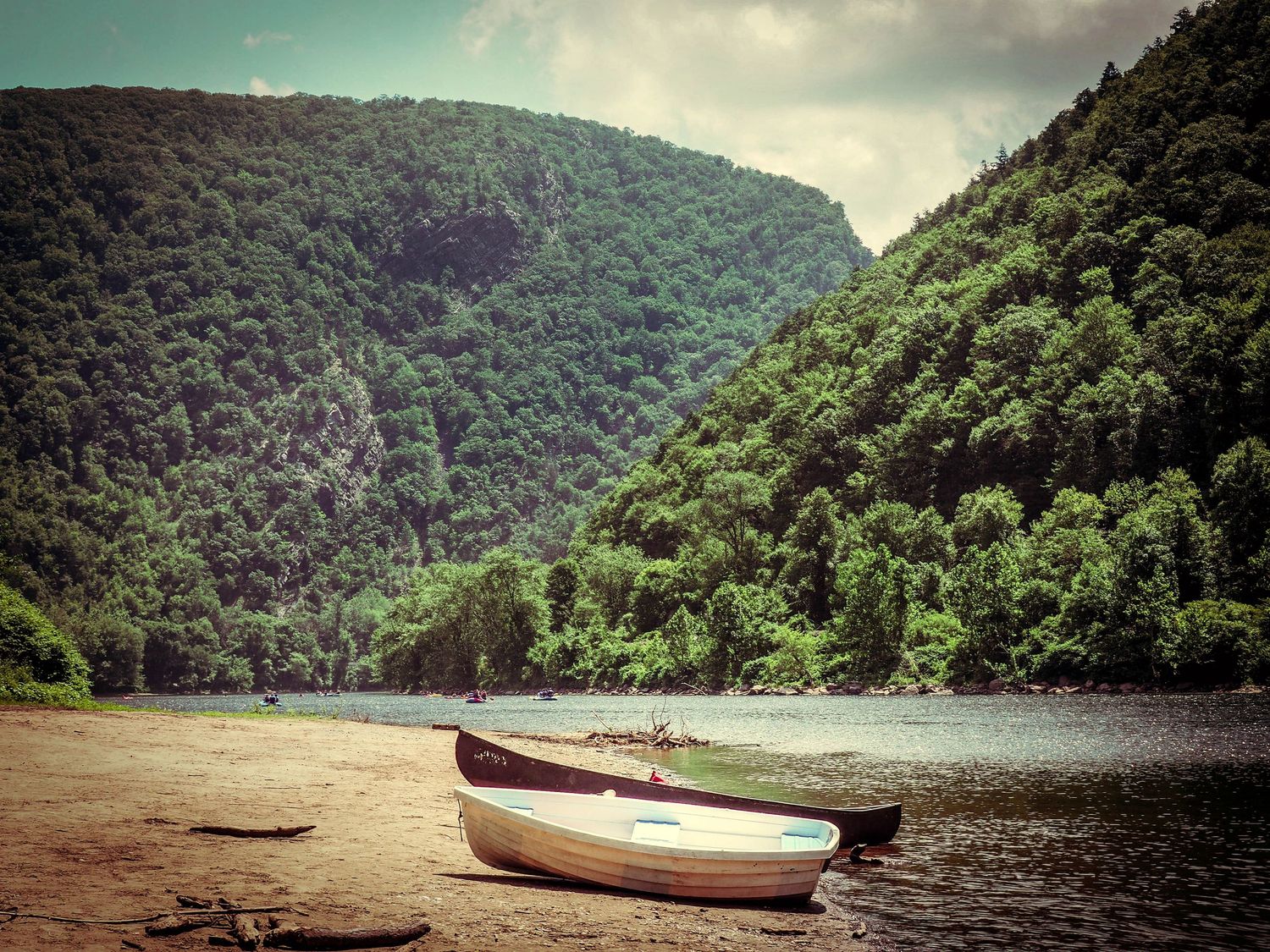 Two canoes rest on a beach by a tranquil lake surrounded by steep forested mountains under a moody sky.