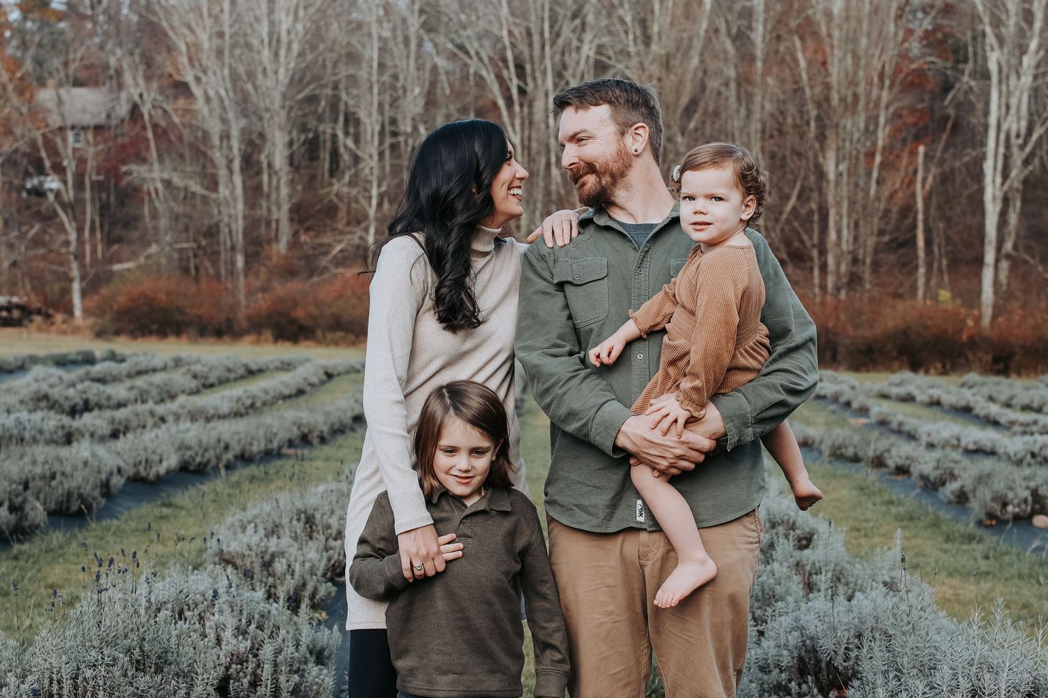 Family wearing coordinated earth tone outfits poses together in autumn garden with lavender plants.