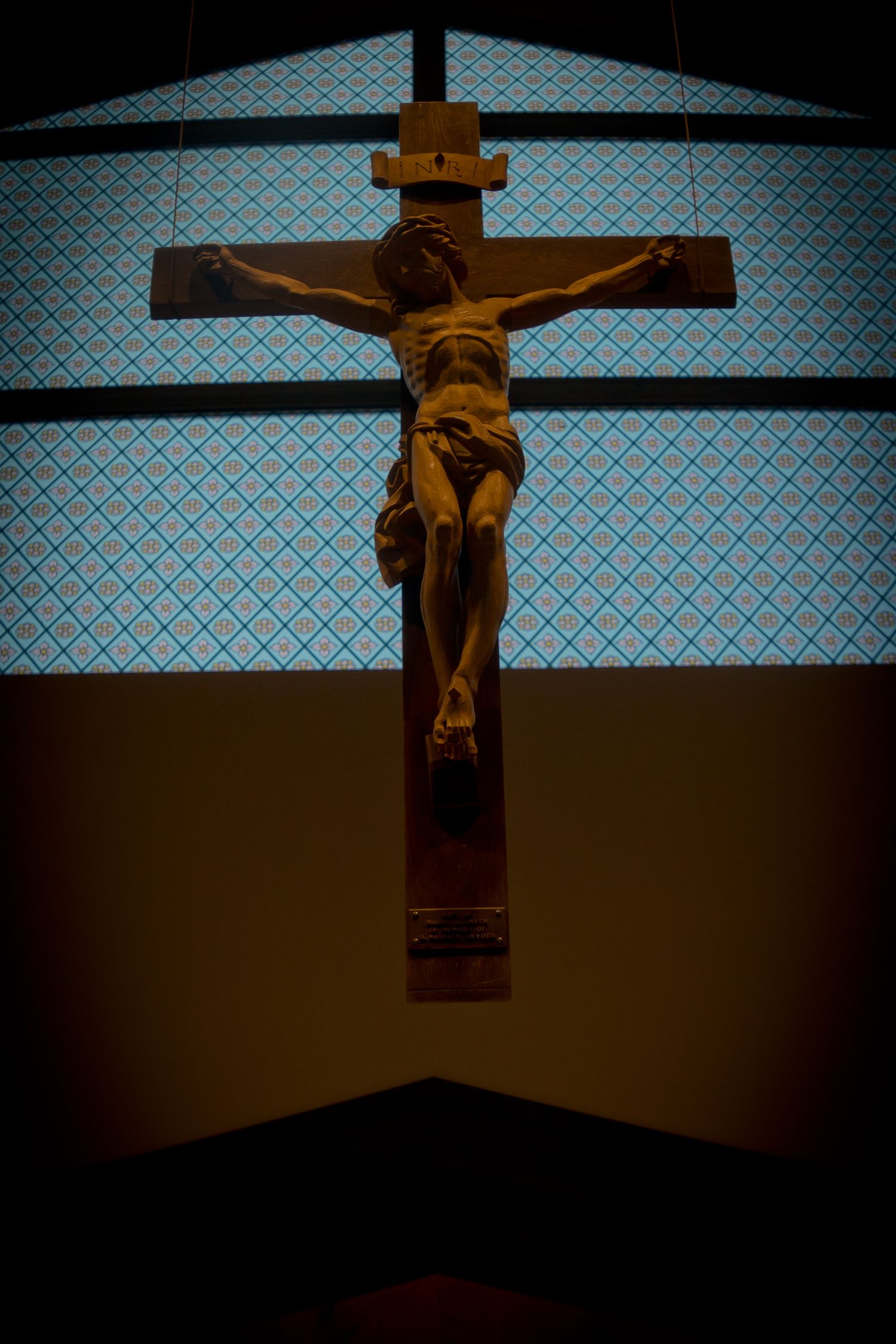 A wooden crucifix silhouetted against a blue patterned background in dramatic lighting.