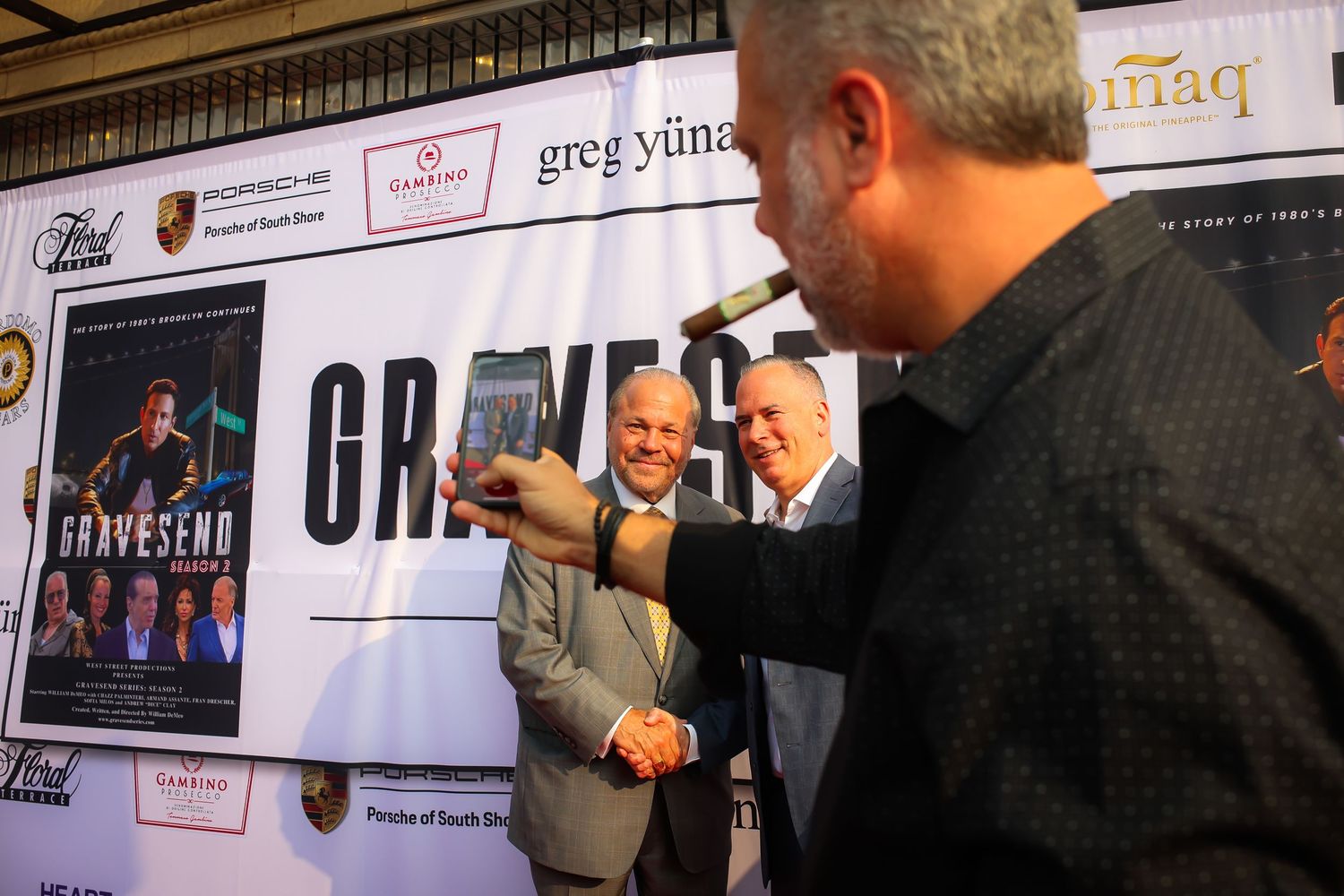 People interact at a promotional event with a backdrop featuring movie posters and sponsor logos.