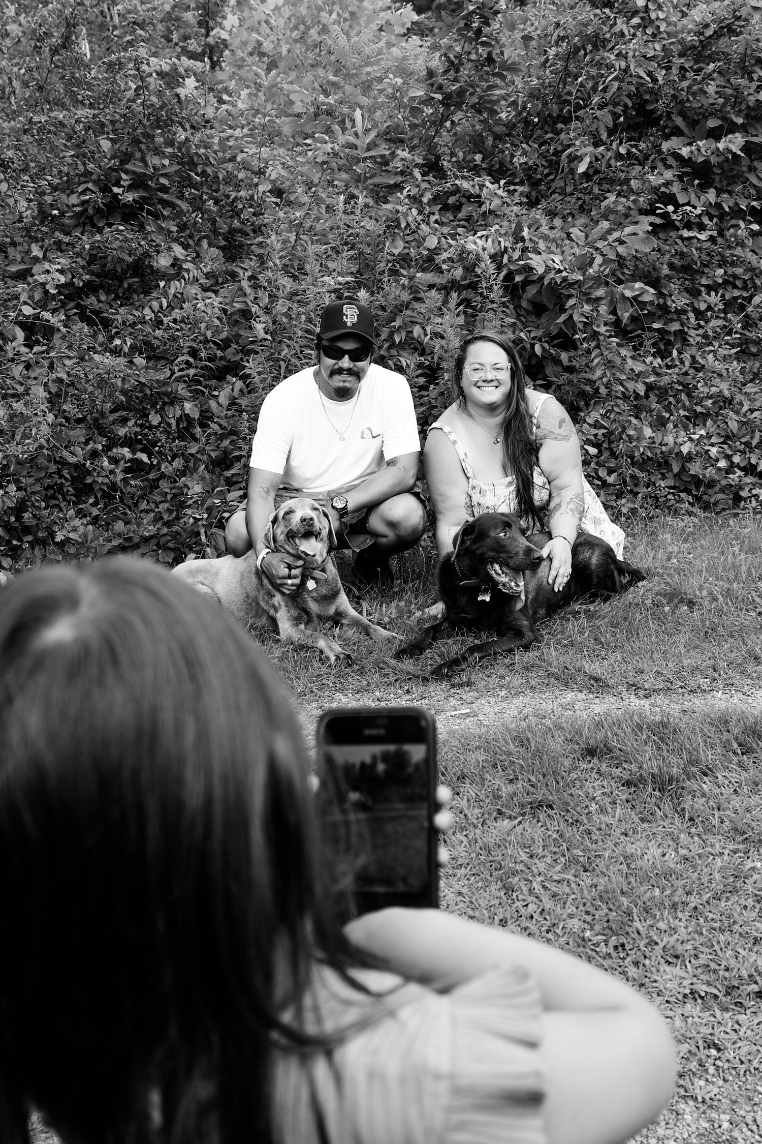A group of people and a dog sit together on a grassy hill in a black and white photograph.