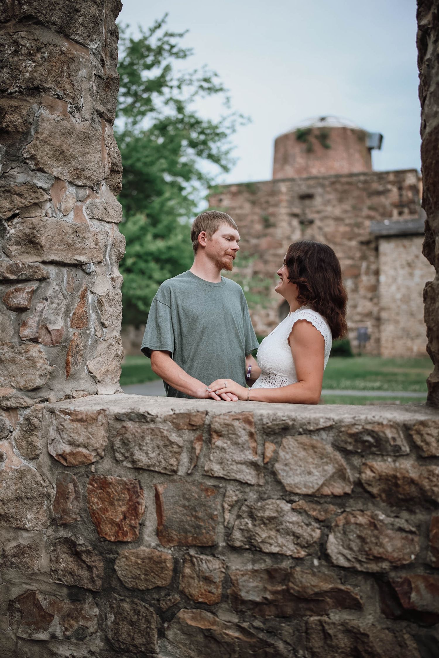 Couple holding hands at historic stone ruins, gazing at each other romantically outdoors.