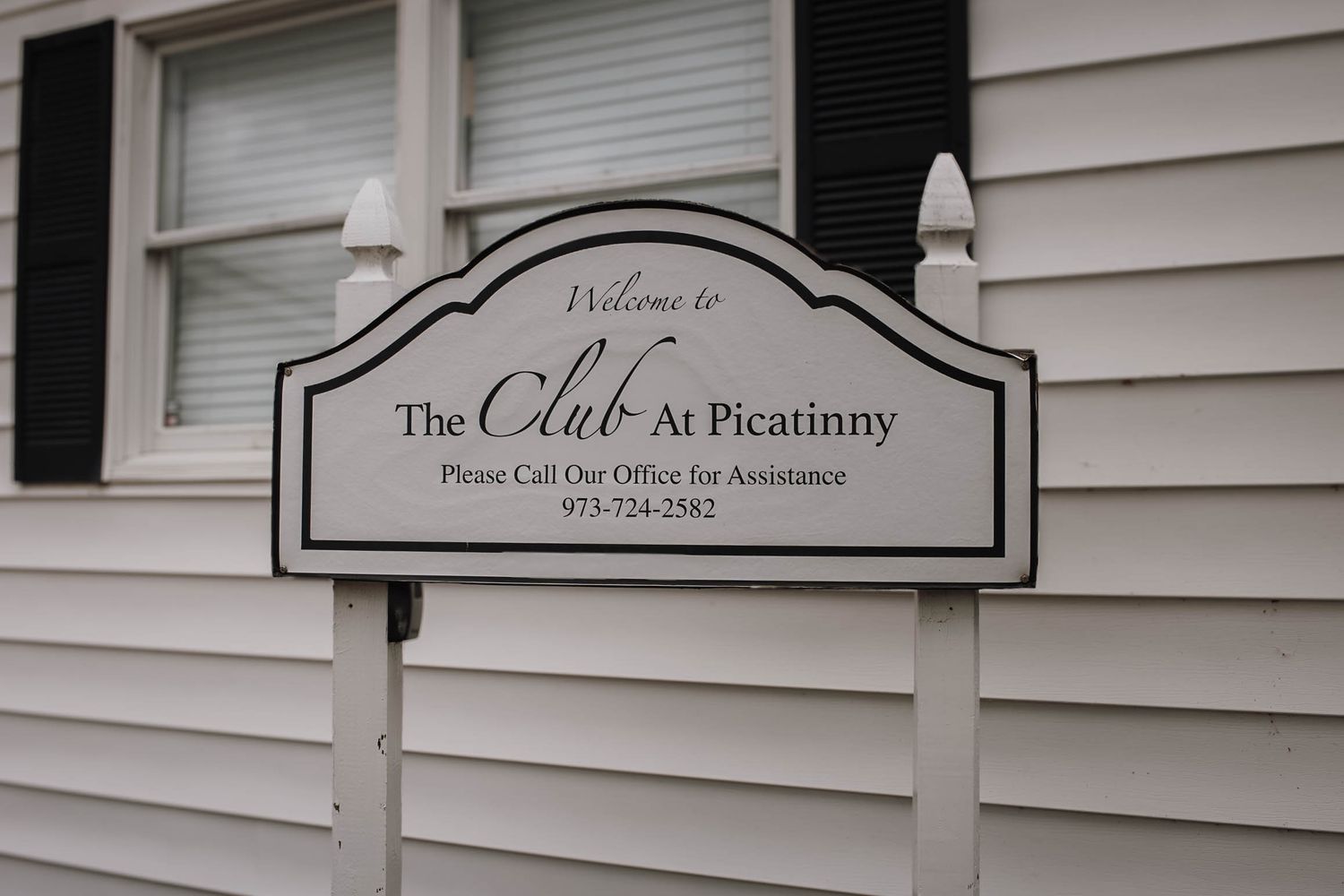 Welcome sign for The Club at Picatinny with contact number 973-724-2582 on white siding.