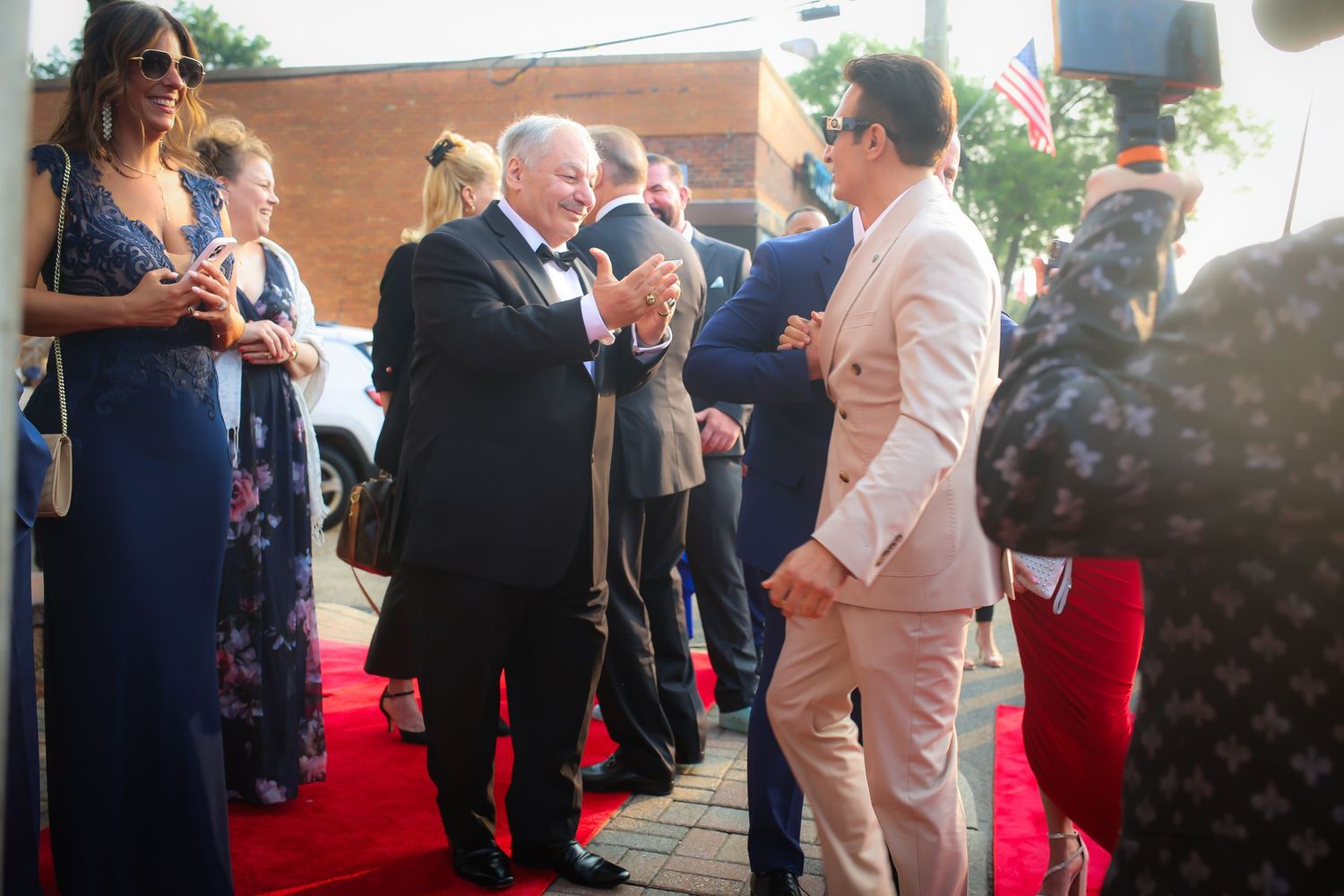 People gather at a formal event with a red carpet, some holding phones and taking photos.