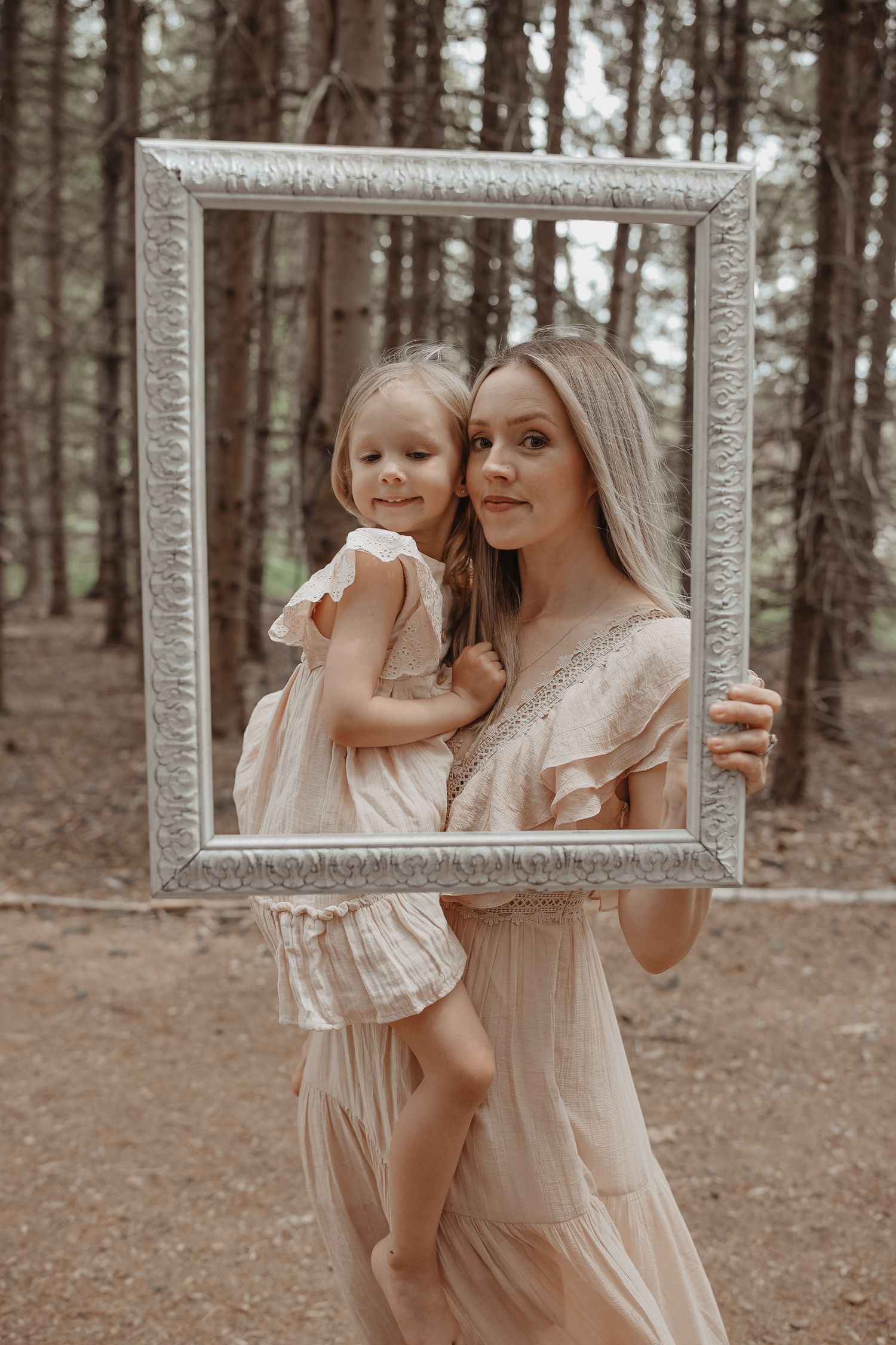 A rustic forest photoshoot featuring a decorative white frame held up in different poses against a wooded backdrop.