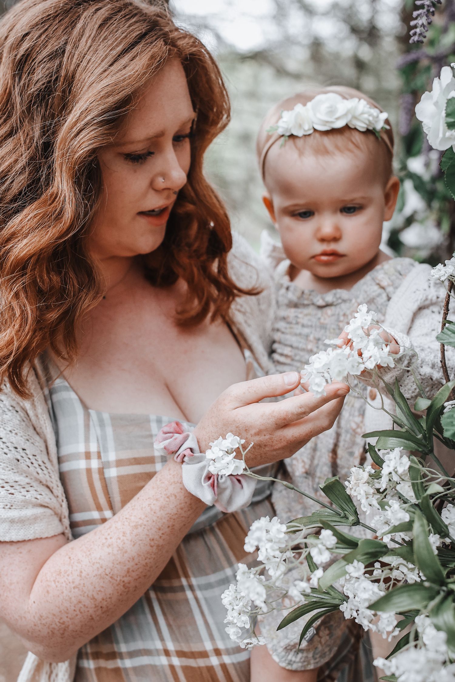 A tender moment captured in soft tones as mother and baby explore delicate white spring blossoms together.