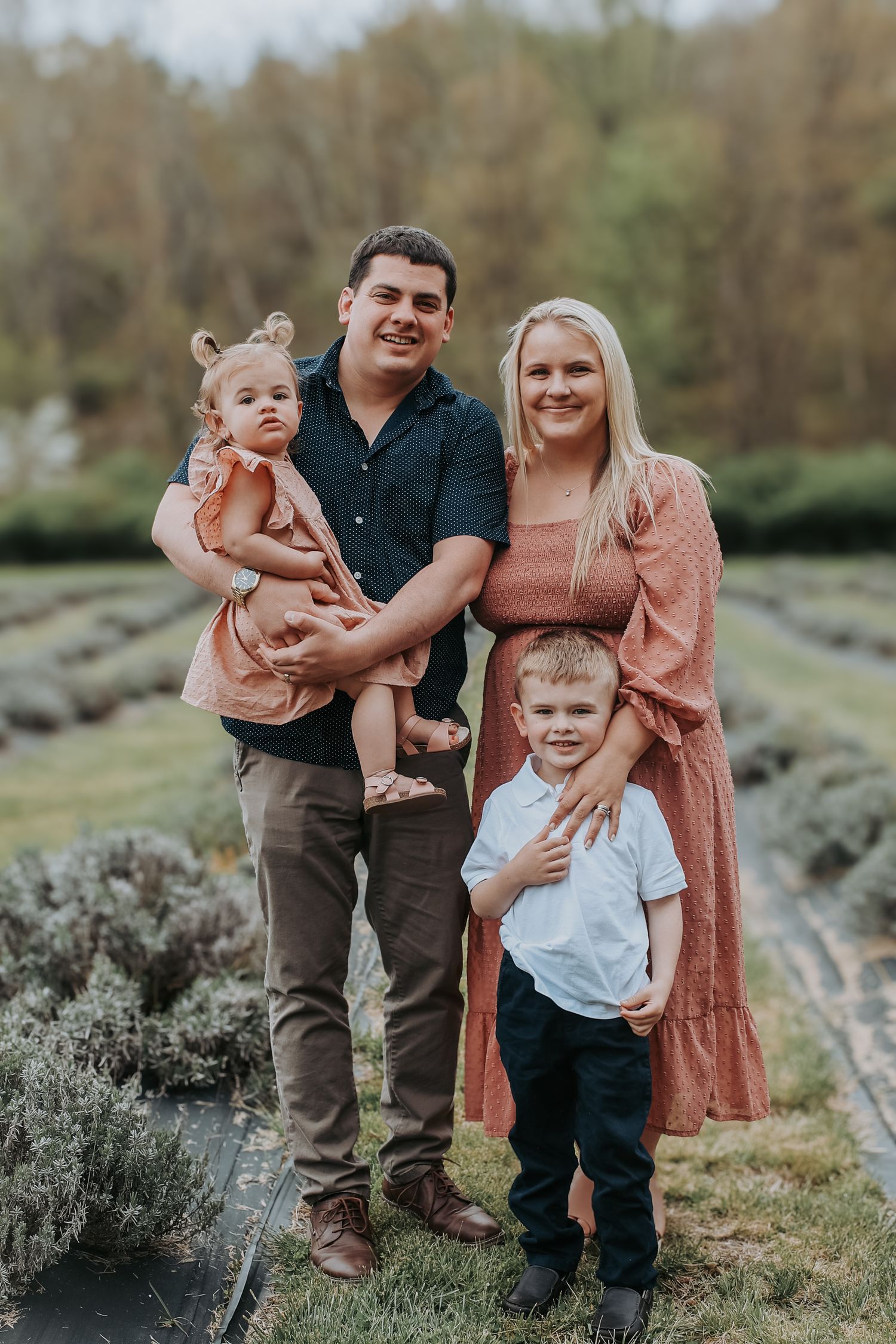 Family in coordinating earth-tone outfits poses together outdoors against natural foliage backdrop.