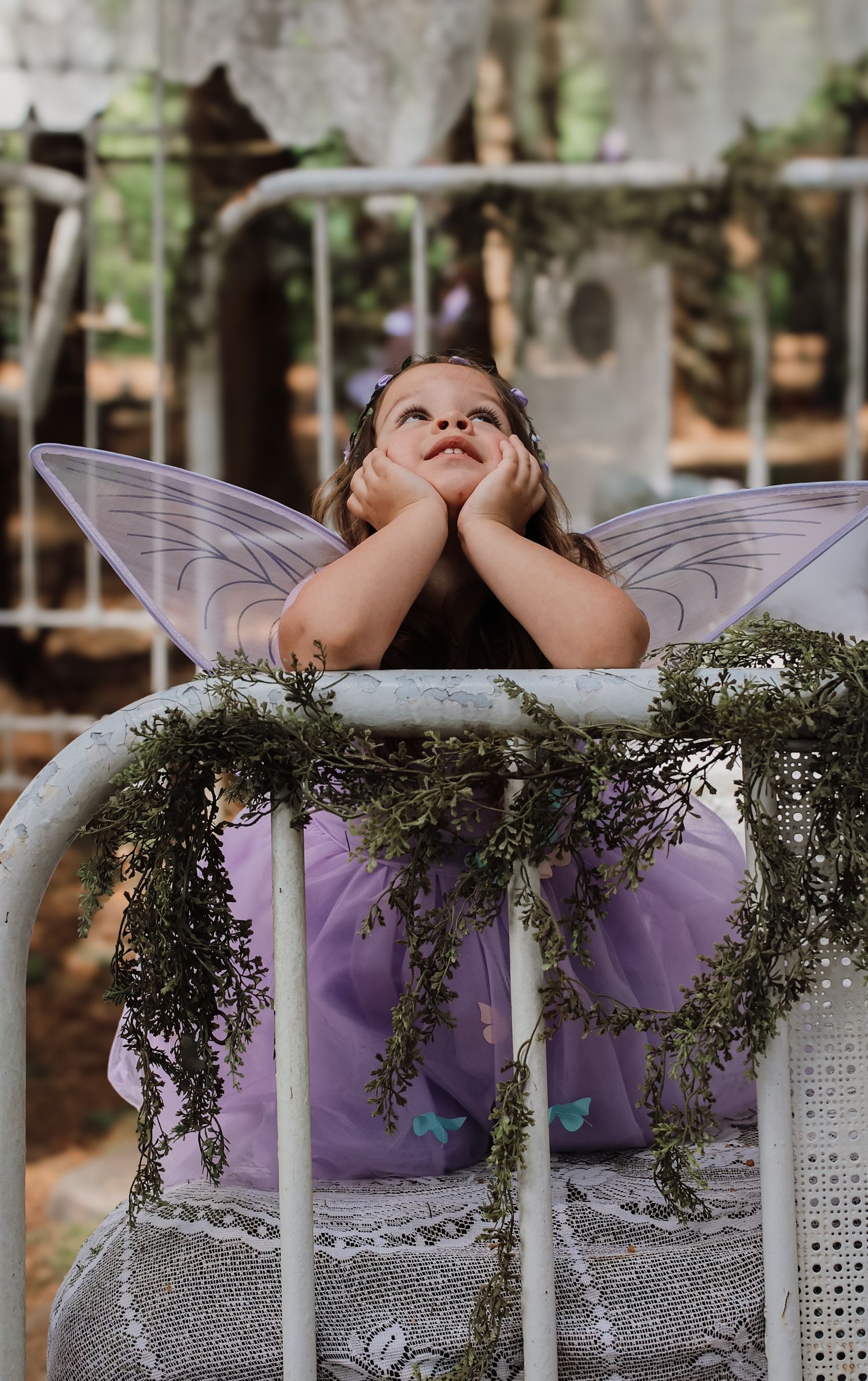 A child wearing fairy wings lies on a white bench decorated with greenery and floral arrangements.