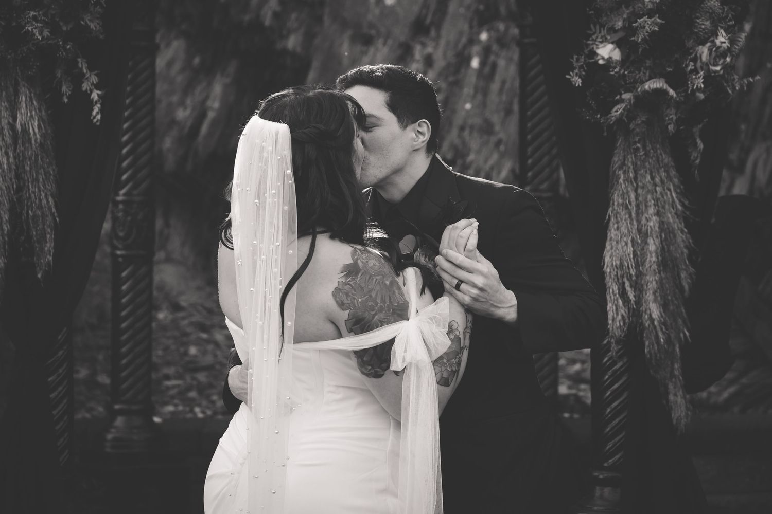 A bride and groom share an intimate moment during their wedding ceremony in a rustic outdoor setting.