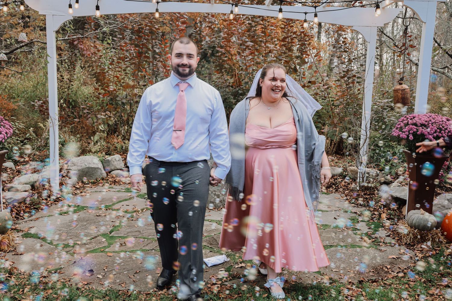 People celebrating outdoors with pink confetti and bubbles in a garden setting during a special event.