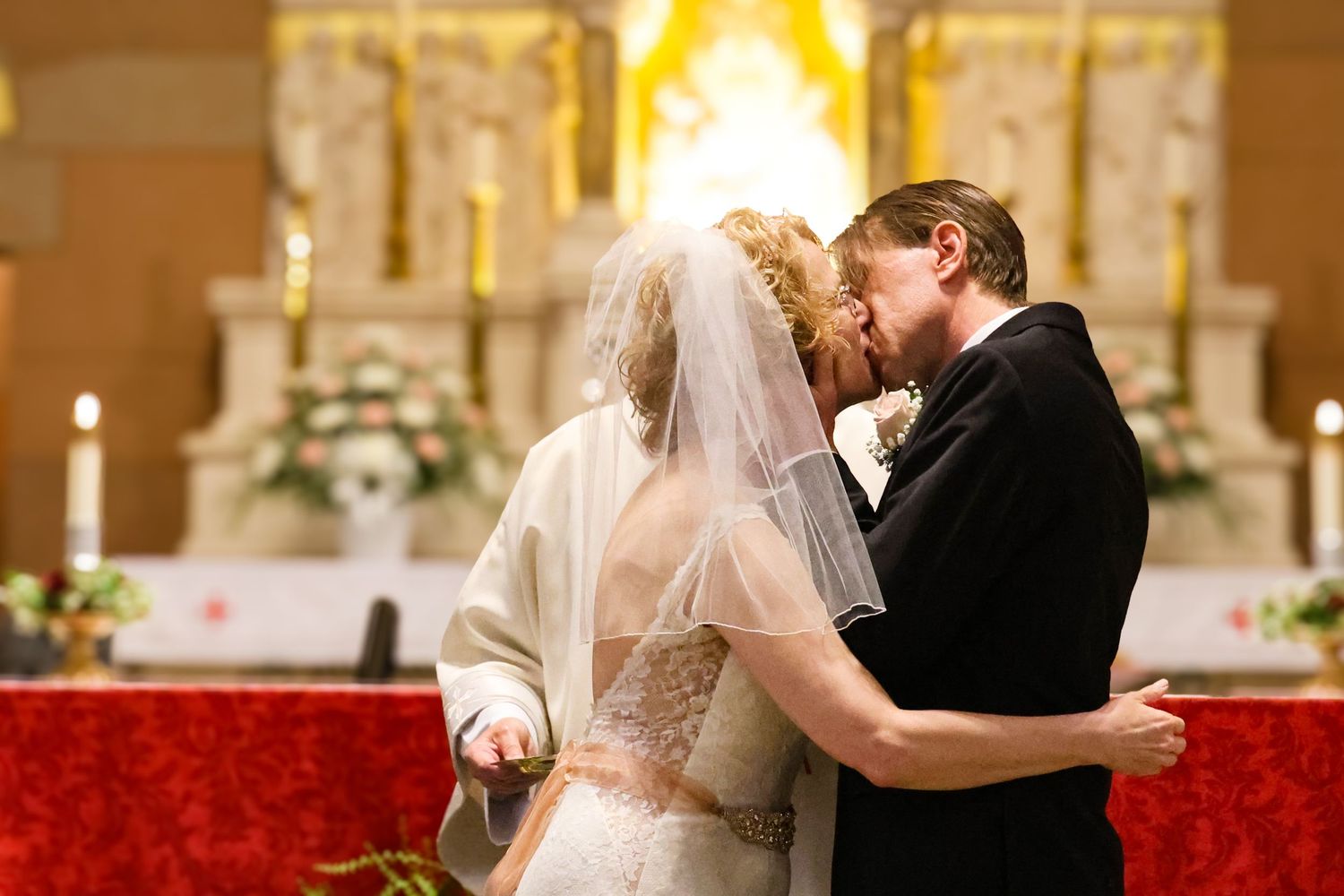 A wedding couple shares their first kiss at the altar surrounded by red poinsettias and holiday decorations.