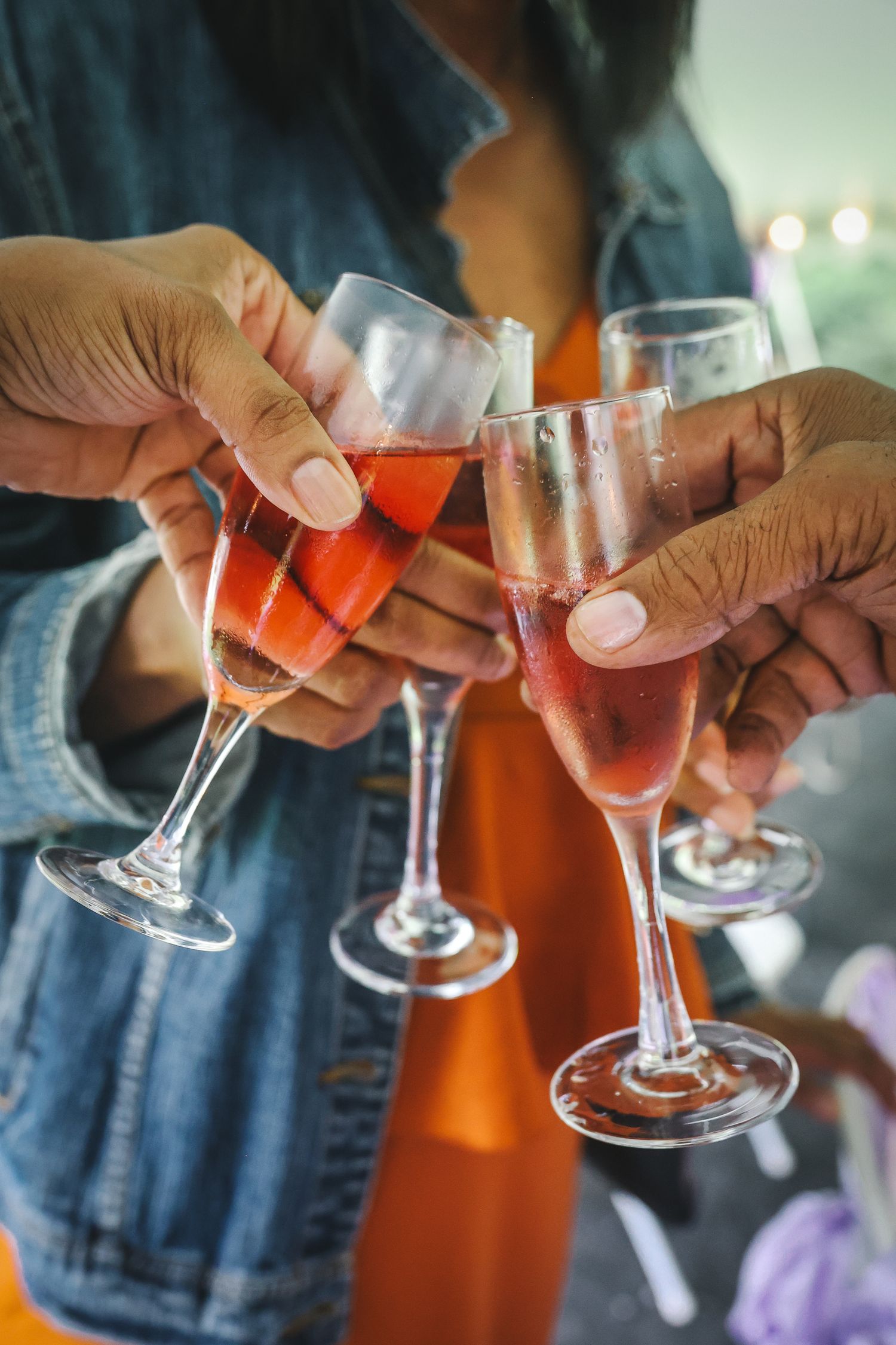 Multiple hands clink champagne glasses together in a celebratory toast sequence against an orange background.