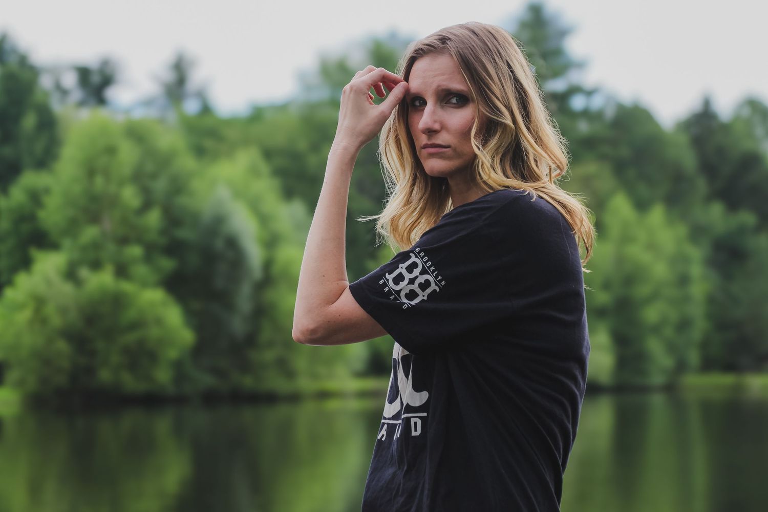 A person in a black shirt poses thoughtfully against a scenic lake and forest backdrop.