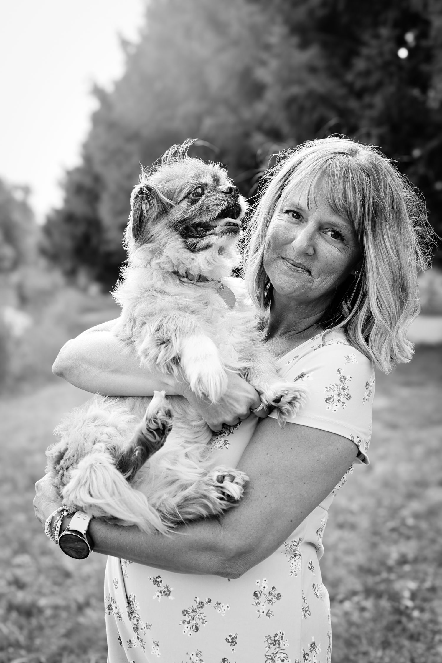 A series of black and white photos showing a person in a floral dress joyfully playing with a small fluffy dog outdoors.