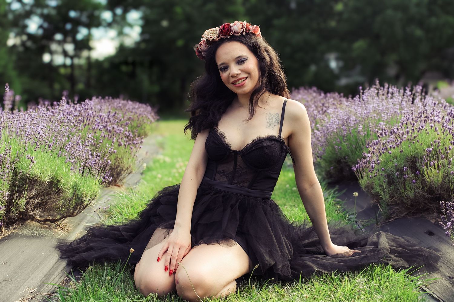 A figure in a black tulle dress poses gracefully among blooming lavender flowers in a garden setting.