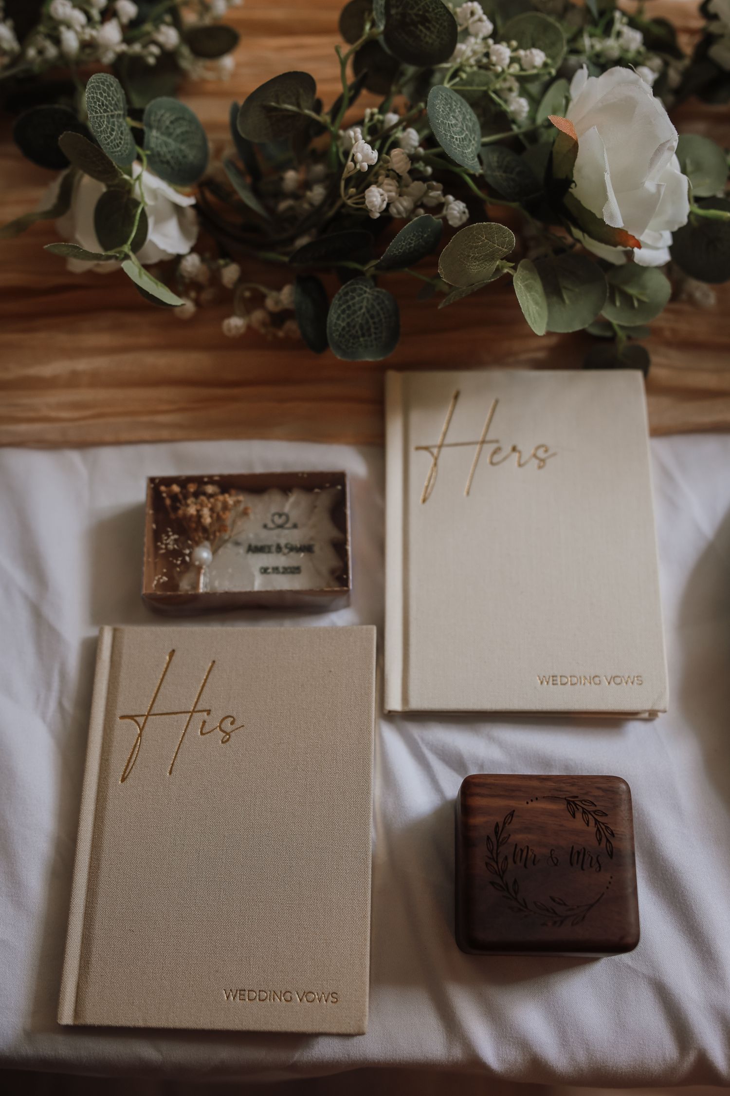 Wedding rings and gift boxes arranged on white linen with eucalyptus leaves and delicate decorative details.