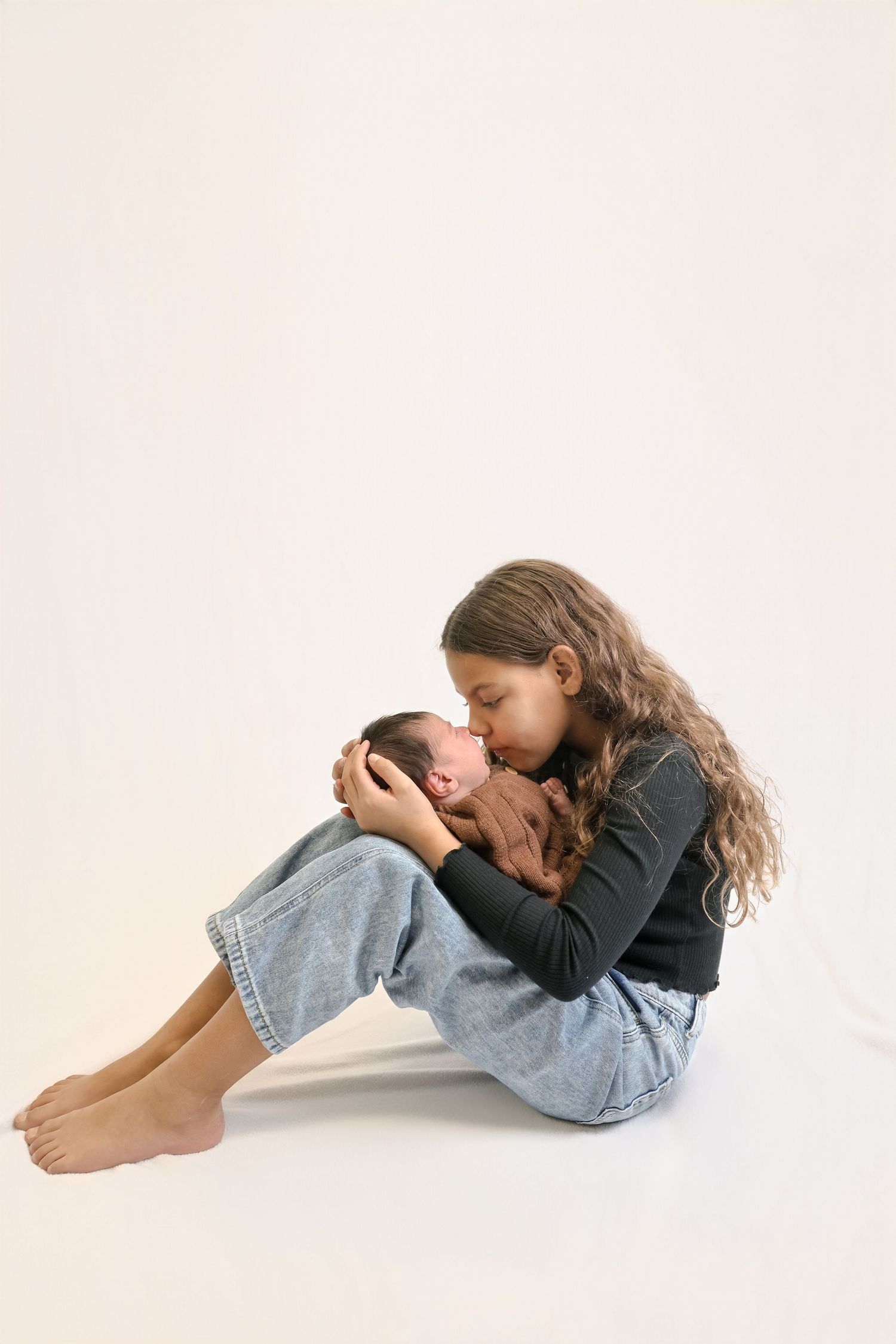 Person curled up in fetal position wearing denim jeans and black sweater lying on white background.