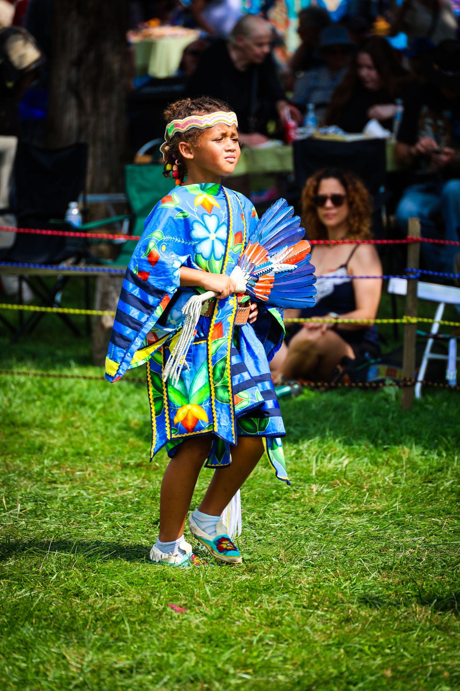 A performer in a vibrant tie-dye outfit dances on grass during an outdoor festival event.