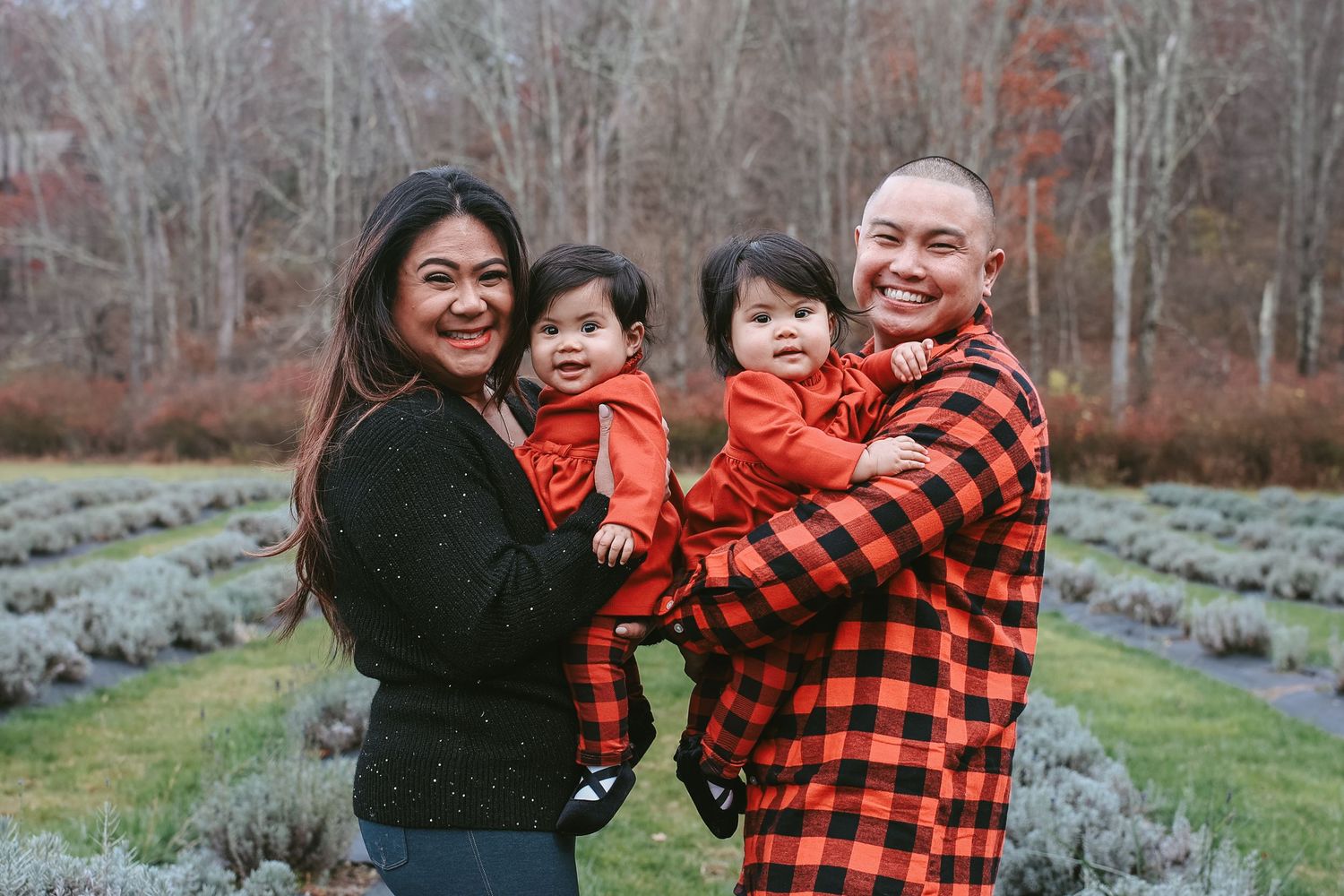 Family wearing matching black and red buffalo plaid outfits poses together in an outdoor garden setting.