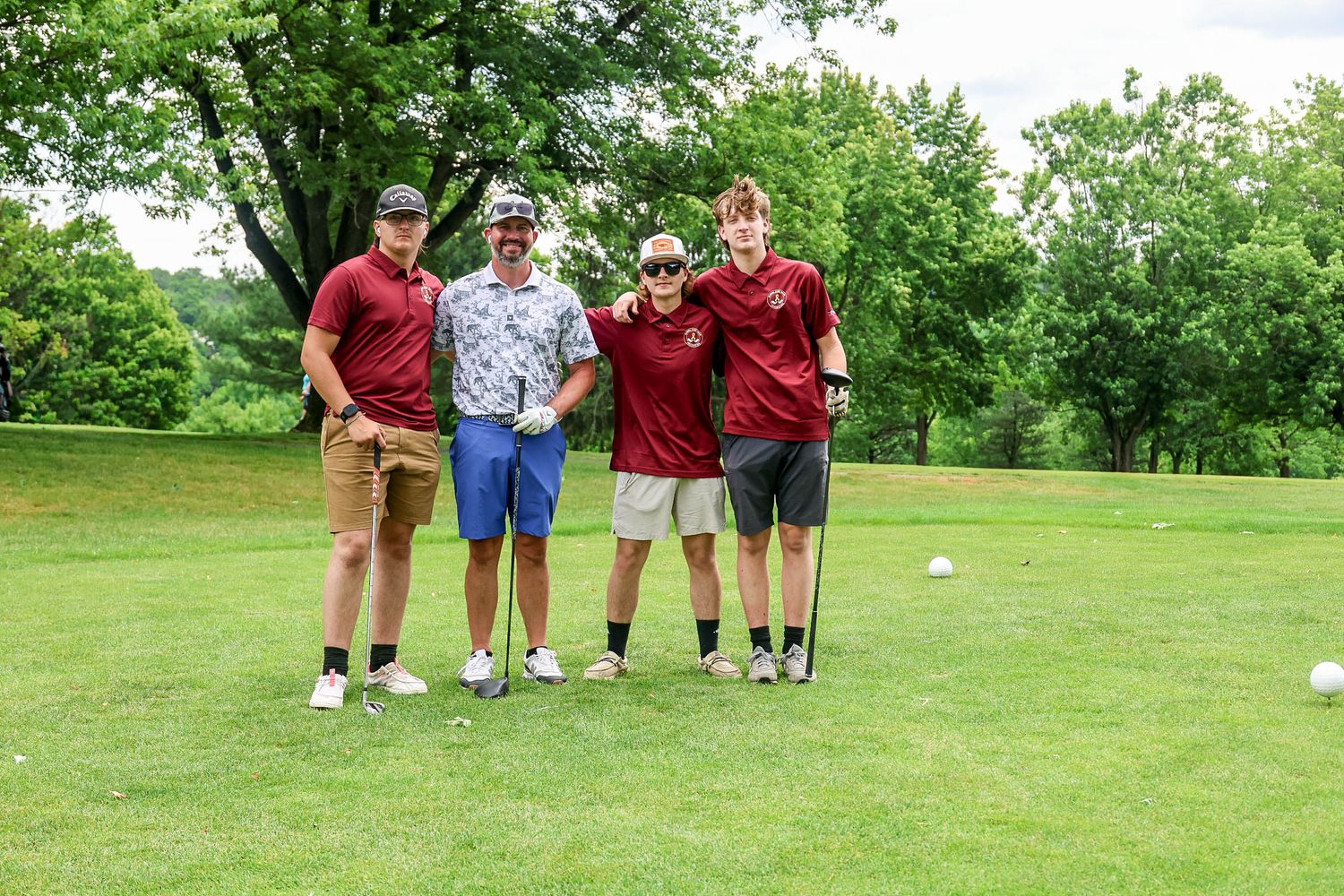 Four golfers posing together on a lush green golf course on a cloudy summer day.