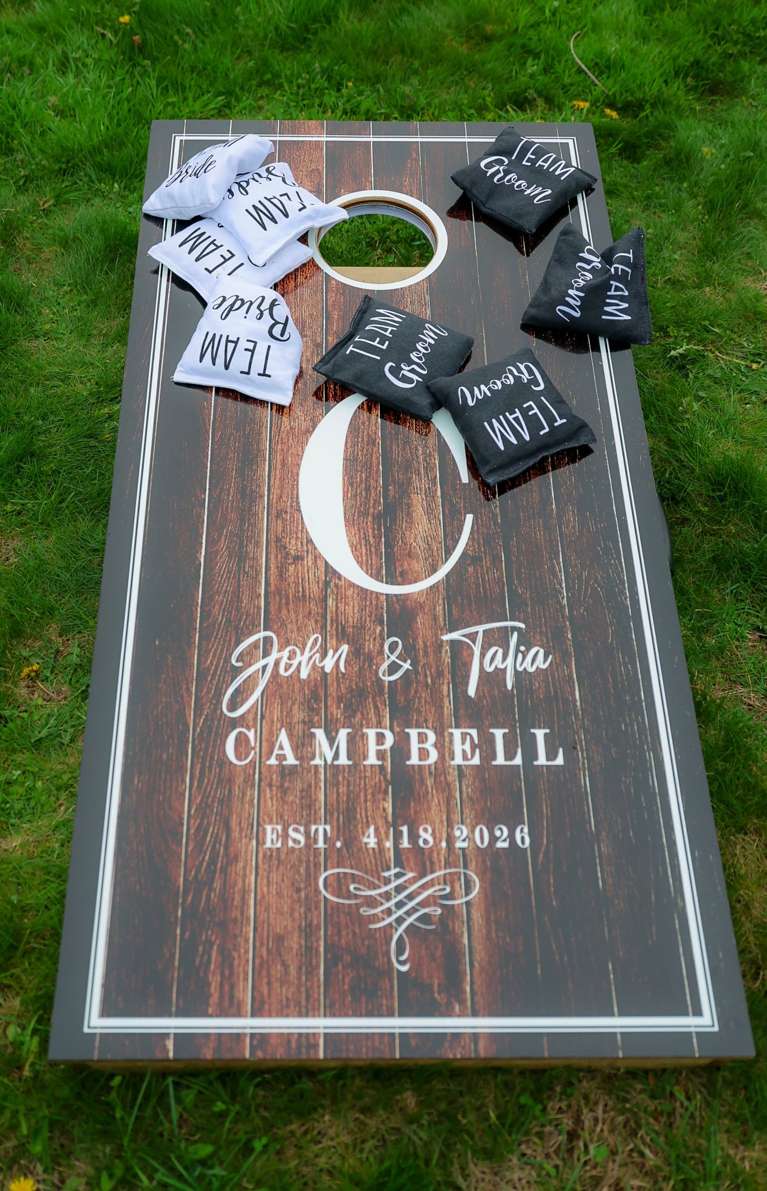 Personalized cornhole board for John & Talia Campbell EST. 4.18.2026 with Team Bride and Team Groom bean bags.